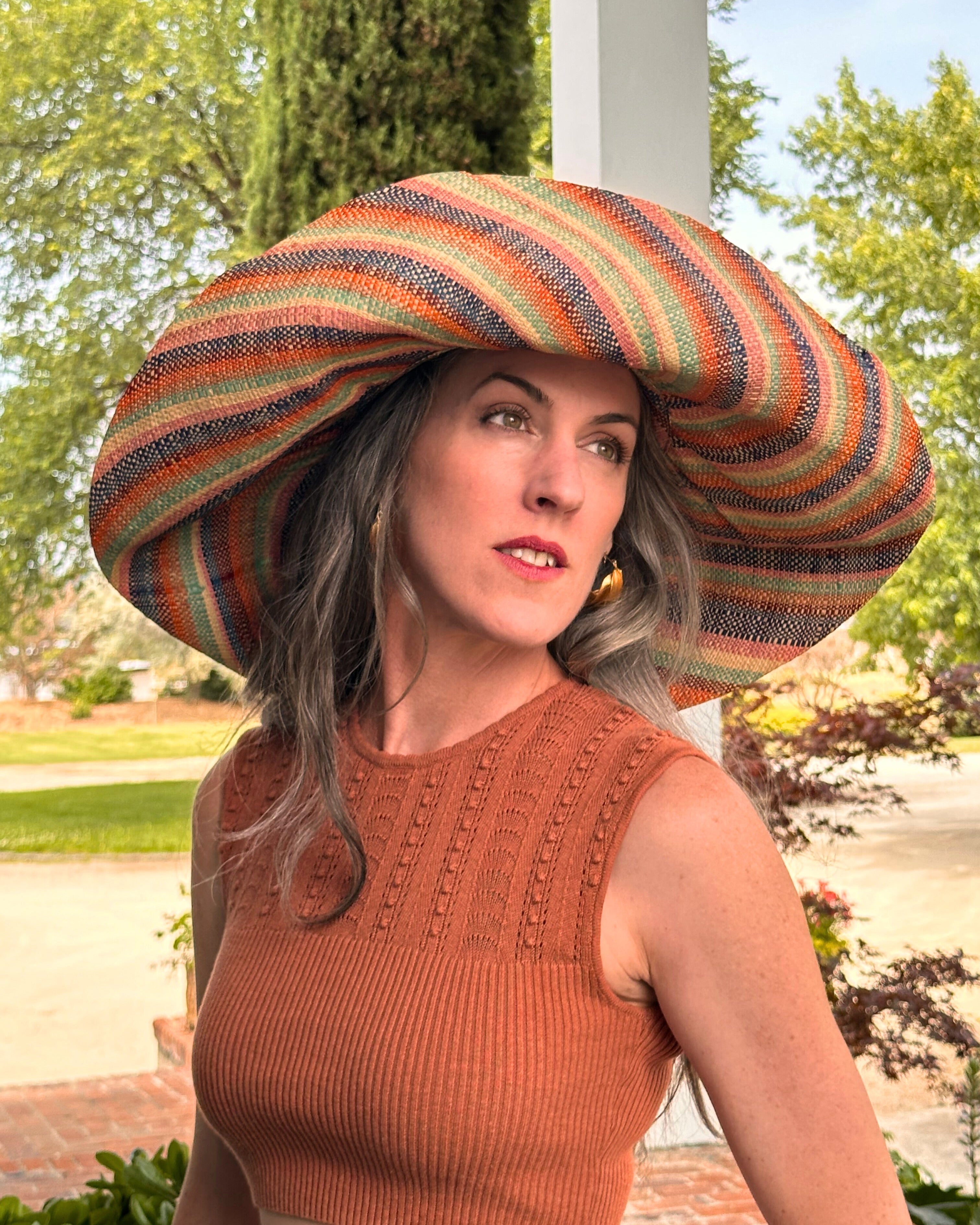 Model wearing 5Monica 7" Wide Brim Taffy Multicolor Stripes Packable Straw Sun Hat Handmade loomed raffia in multi width bands of saffron yellow, turquoise blue, seafoam blue/green, orange, pink, bordeaux red, etc., and natural create a swirl pattern - Shebobo