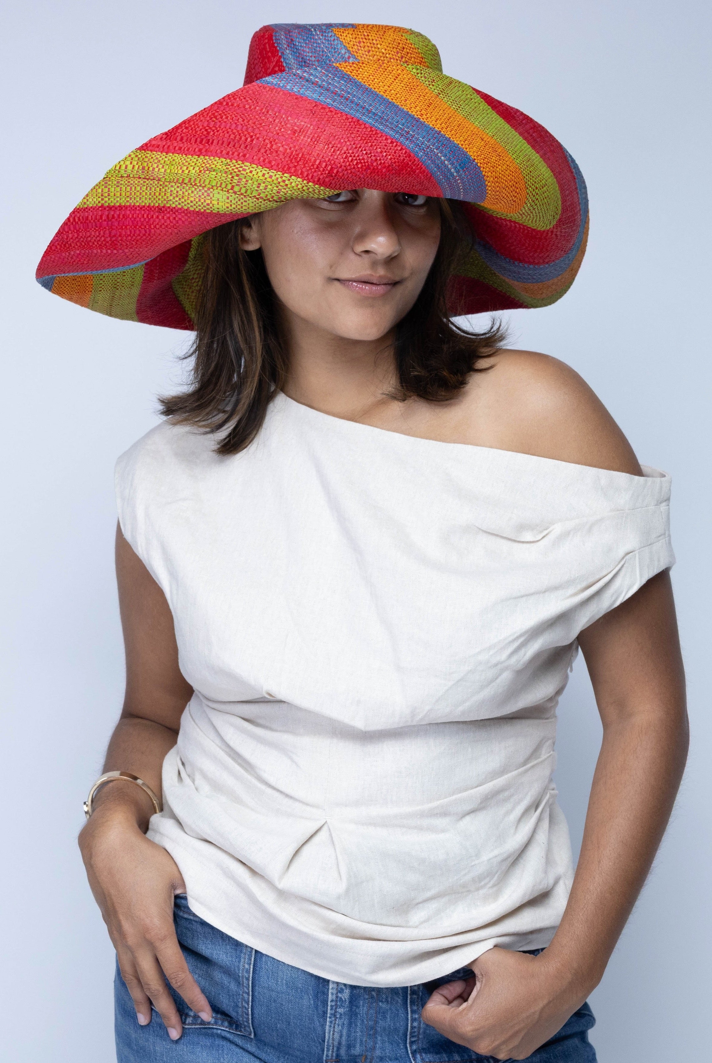 Model wearing Monica 7" Wide Brim Na Pali Swirl Multicolor Stripes Packable Straw Sun Hat handmade loomed raffia in bands of red, saffron yellow/orange, midori lime/green, and denim retro/light/blue stripes create a swirl pattern - Shebobo