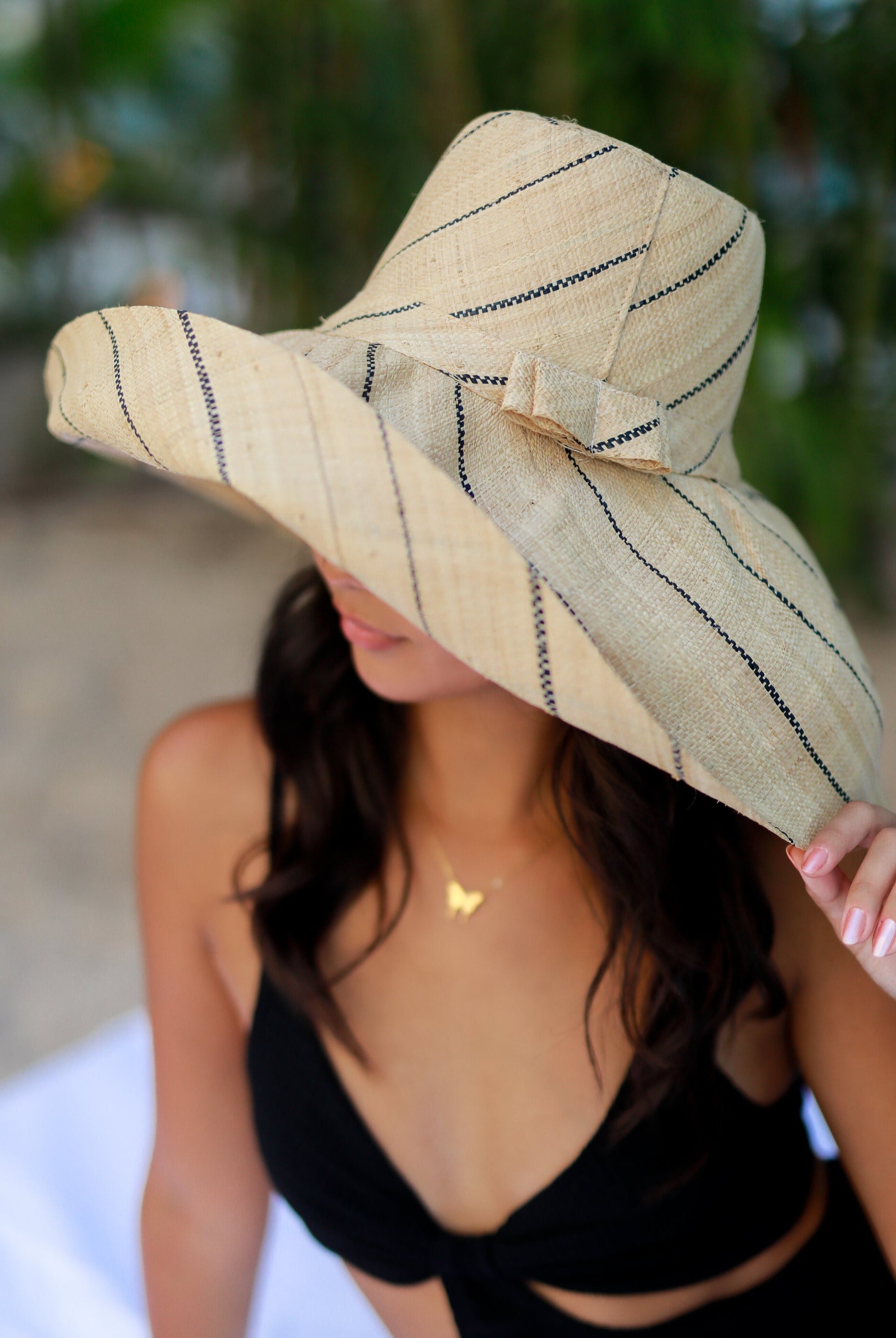 Model wearing Monica 7" Wide Brim Natural Pinstripes Packable Straw Sun Hat handmade loomed raffia in wide bands of natural straw color with narrow bands of black create a striped swirl pattern - Shebobo