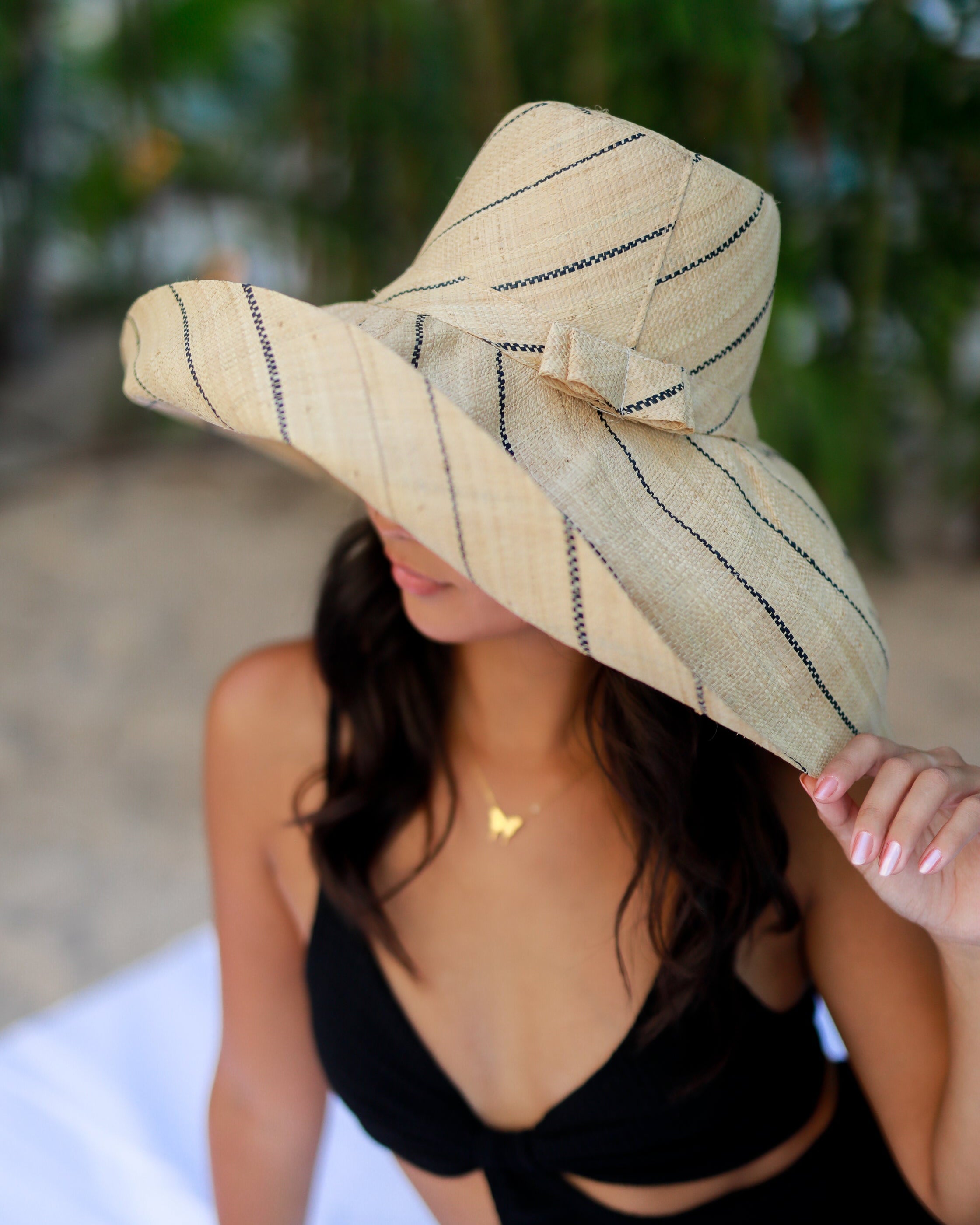 Model wearing Monica 7" Wide Brim Natural Pinstripes Packable Straw Sun Hat handmade loomed raffia in wide bands of natural straw color with narrow bands of black create a striped swirl pattern - Shebobo