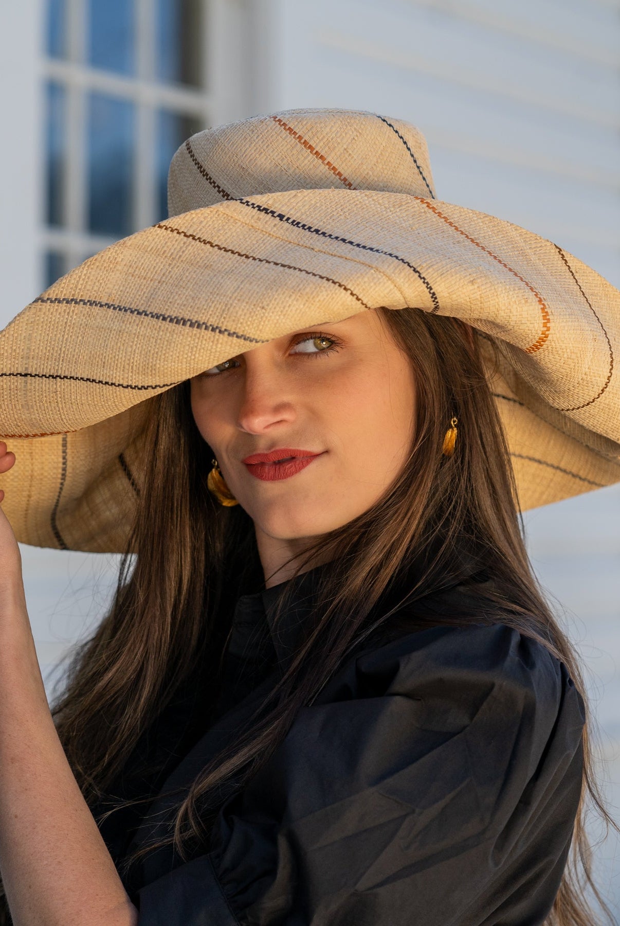 Model wearing Monica 7" wide brim natural and Neutrals multicolor pinstripes packable raffia straw hat handmade loomed raffia in wide bands of natural straw color with narrow bands of blush orange/pink, cinnamon/tobacco/brown, black, and grey create a stripe swirl pattern - Shebobo