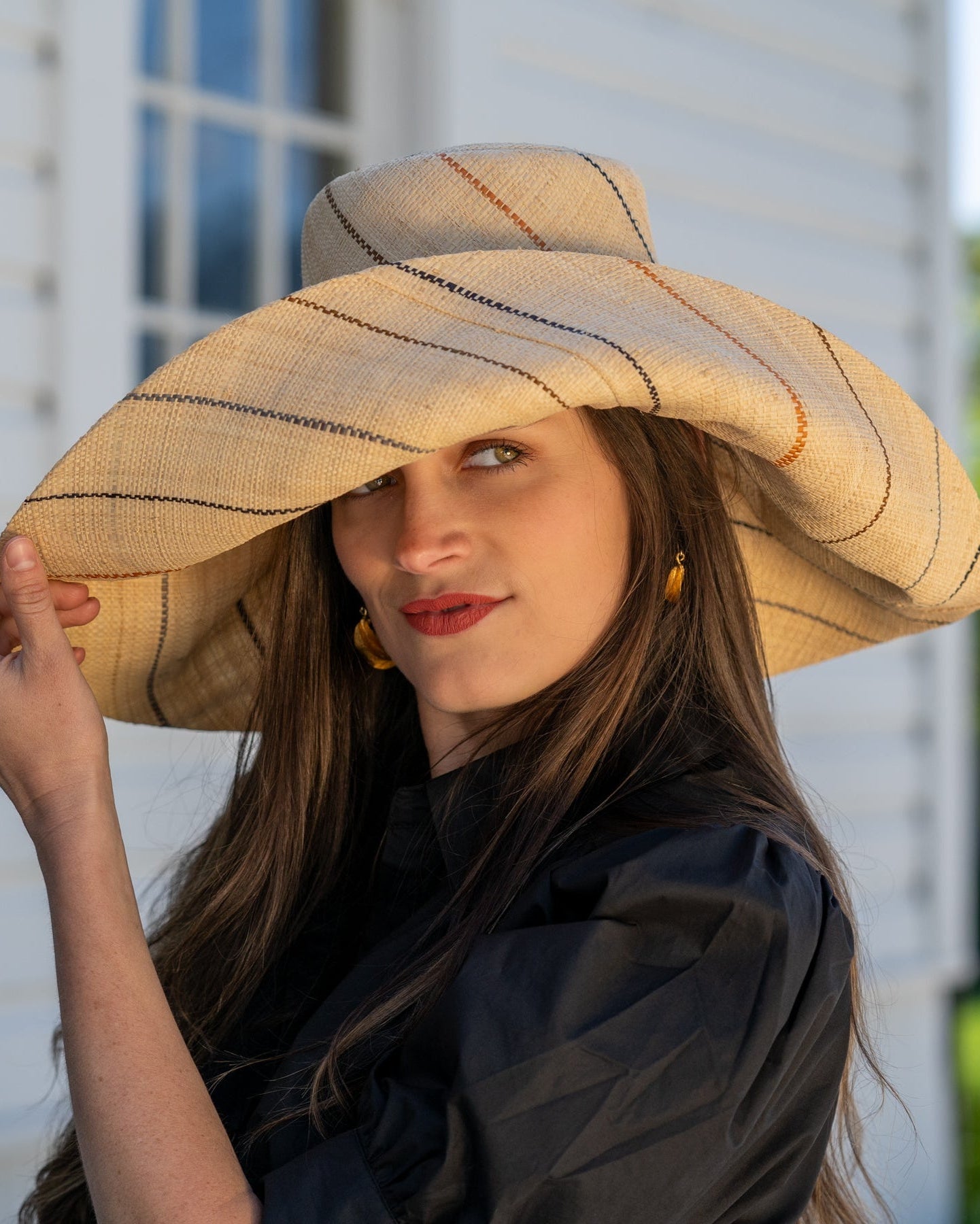 Model wearing Monica 7" wide brim natural and Neutrals multicolor pinstripes packable raffia straw hat handmade loomed raffia in wide bands of natural straw color with narrow bands of blush orange/pink, cinnamon/tobacco/brown, black, and grey create a stripe swirl pattern - Shebobo