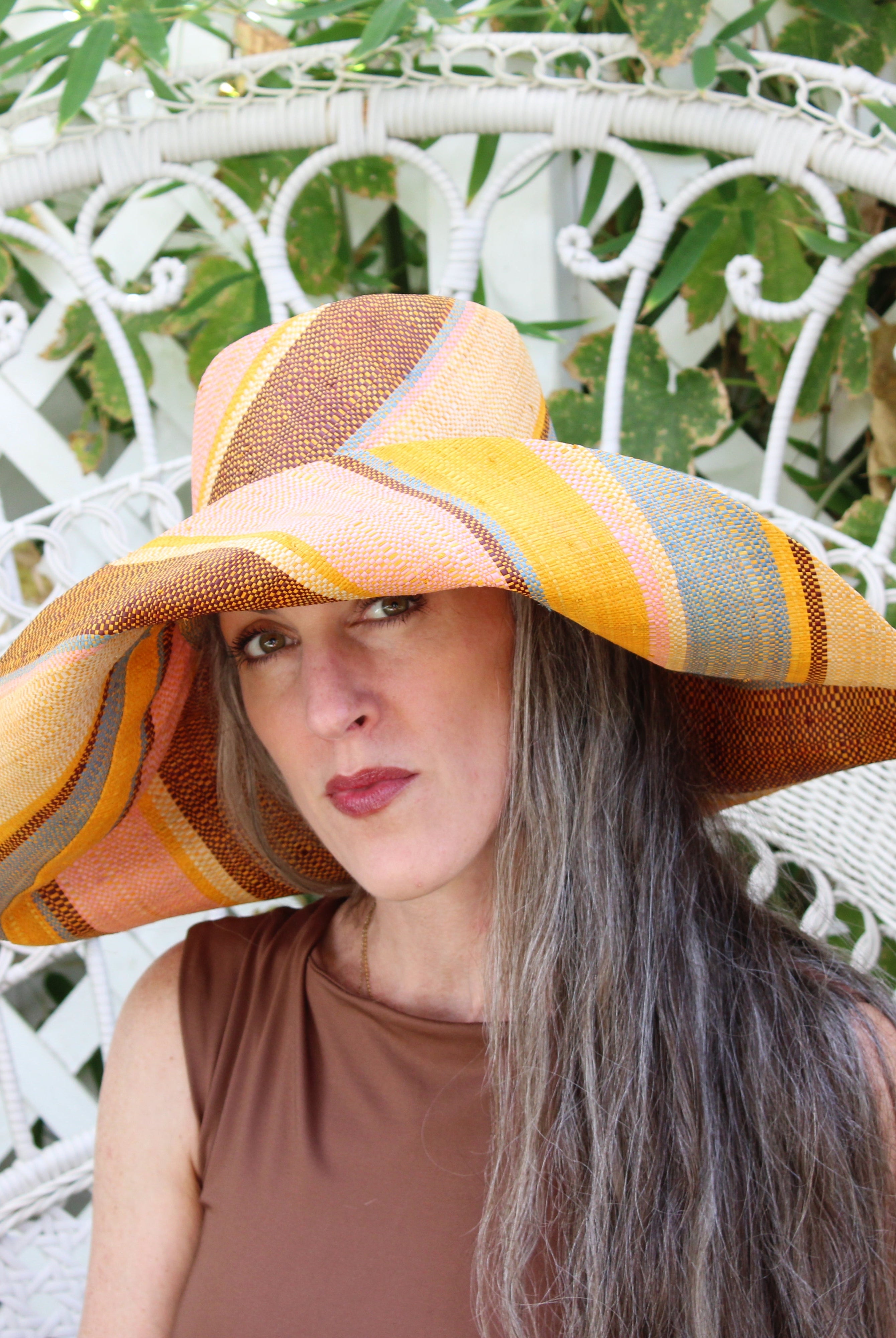 Model wearing Monica 7" Wide Brim Pink Blue Swirl Multicolor Stripes Packable Straw Sun Hat Handmade loomed raffia in multi width bands of saffron yellow, light pink, light blue, black, natural straw color etc. create a swirl pattern - Shebobo