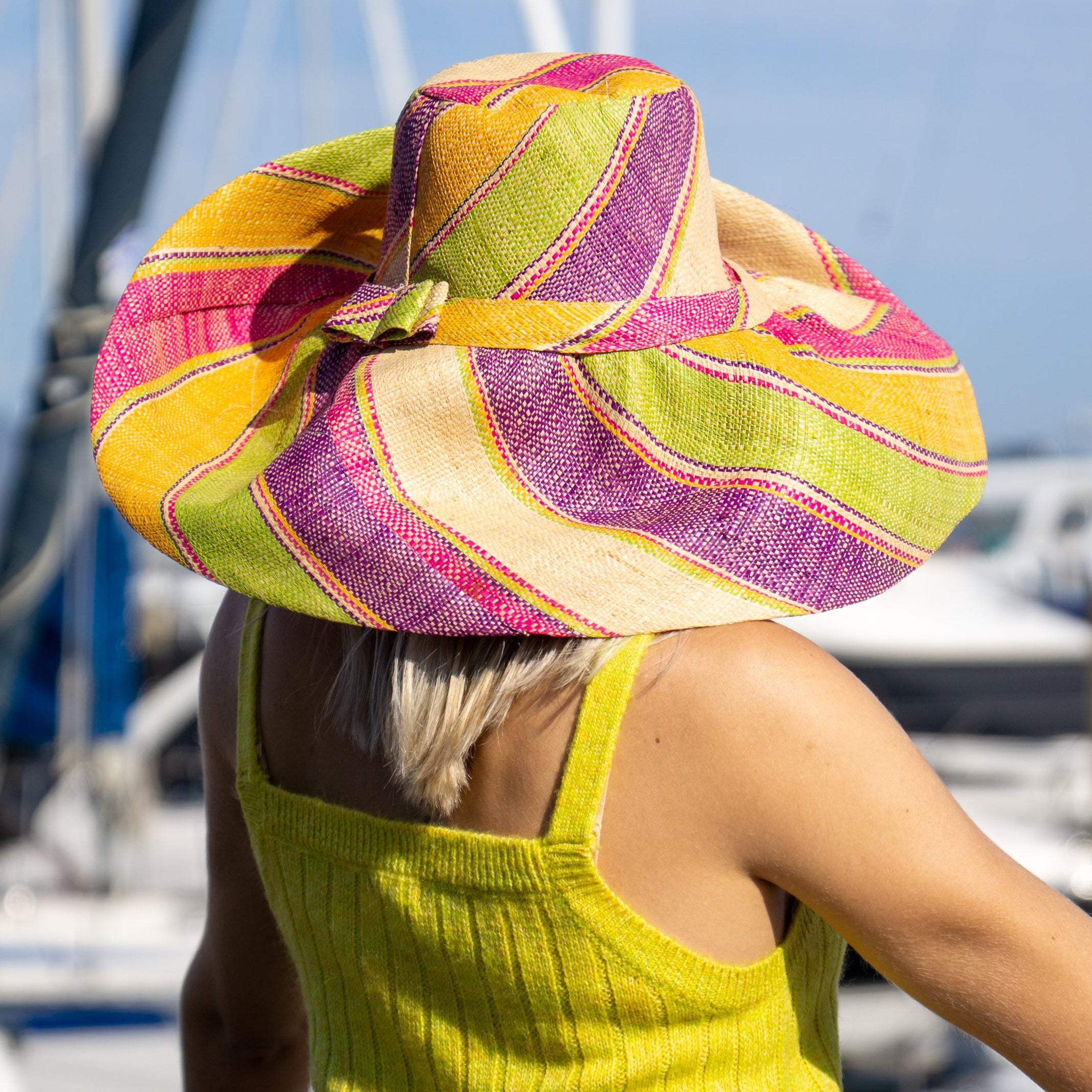Model wearing Monica 7" Wide Brim Pink Lemonade Swirl Multicolor Stripes Packable Straw Sun Hat Handmade loomed raffia in multi width bands of fuchsia pink, purple, yellow, midori lime/green, and natural straw color create a swirl pattern - Shebobo