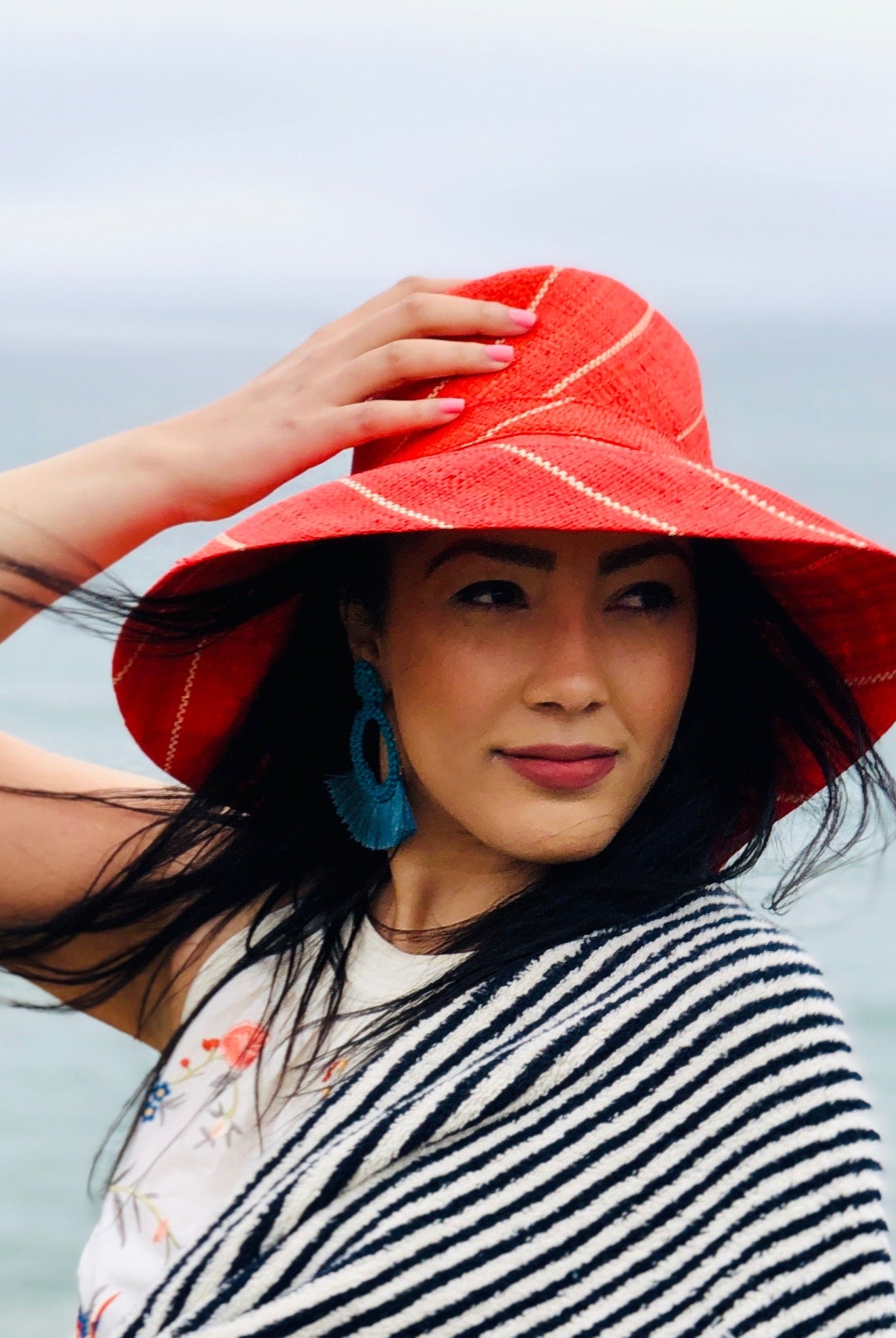 Model wearing Monica 5" Wide Brim Coral Pinstripes Packable Straw Sun Hat handmade loomed raffia in wide stripes of coral red/orange with narrow stripes of natural creating a swirl pattern - Shebobo