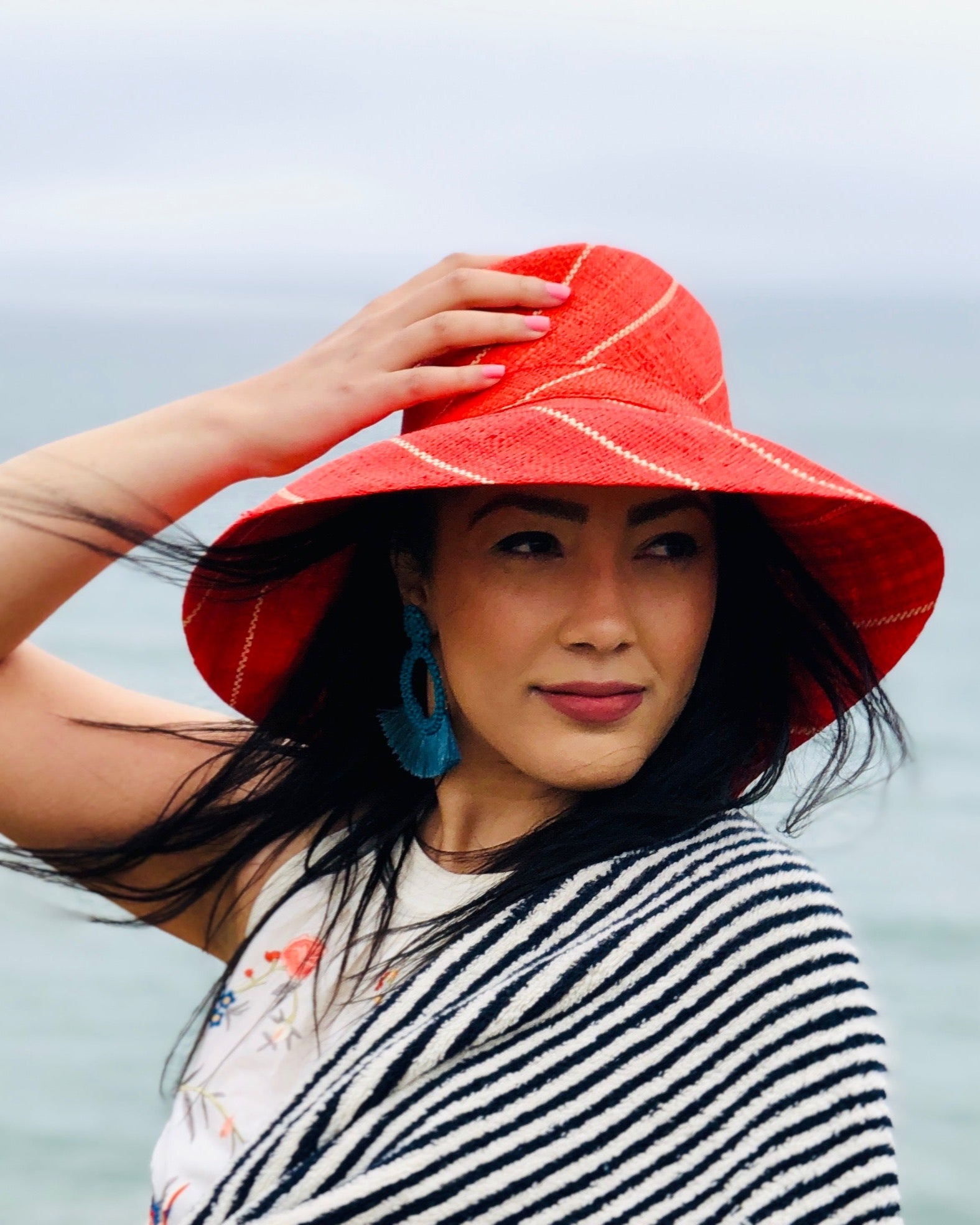 Model wearing Monica 5" Wide Brim Coral Pinstripes Packable Straw Sun Hat handmade loomed raffia in wide stripes of coral red/orange with narrow stripes of natural creating a swirl pattern - Shebobo