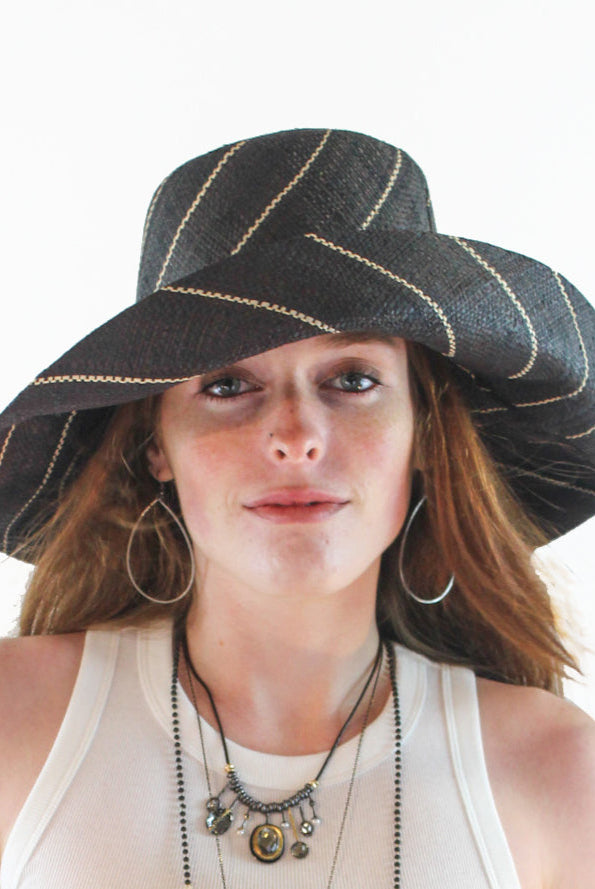 Model wearing Monica 5" Wide Brim Black Pinstripes Packable Straw Sun Hat handmade loomed raffia in wide bands of black with narrow bands of natural straw color create a striped swirl pattern - Shebobo