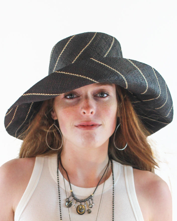 Model wearing Monica 5" Wide Brim Black Pinstripes Packable Straw Sun Hat handmade loomed raffia in wide bands of black with narrow bands of natural straw color create a striped swirl pattern - Shebobo