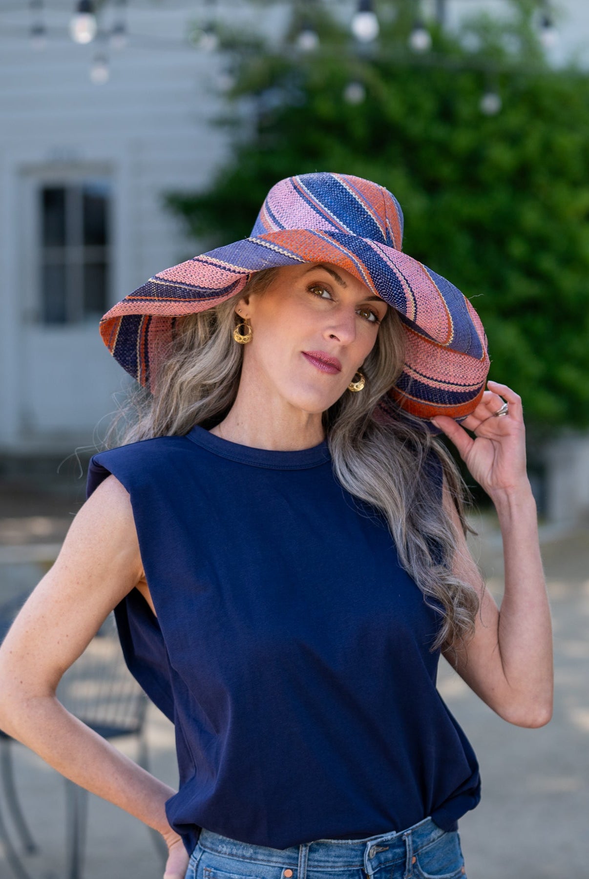 Model wearing Monica 7" Wide Brim Retro Swirl Packable Straw Sun Hat handmade loomed raffia in multi width stripes of denim retro/light/blue, coral orange/red, dusk navy/dark/blue, and light pink create a swirl pattern - Shebobo