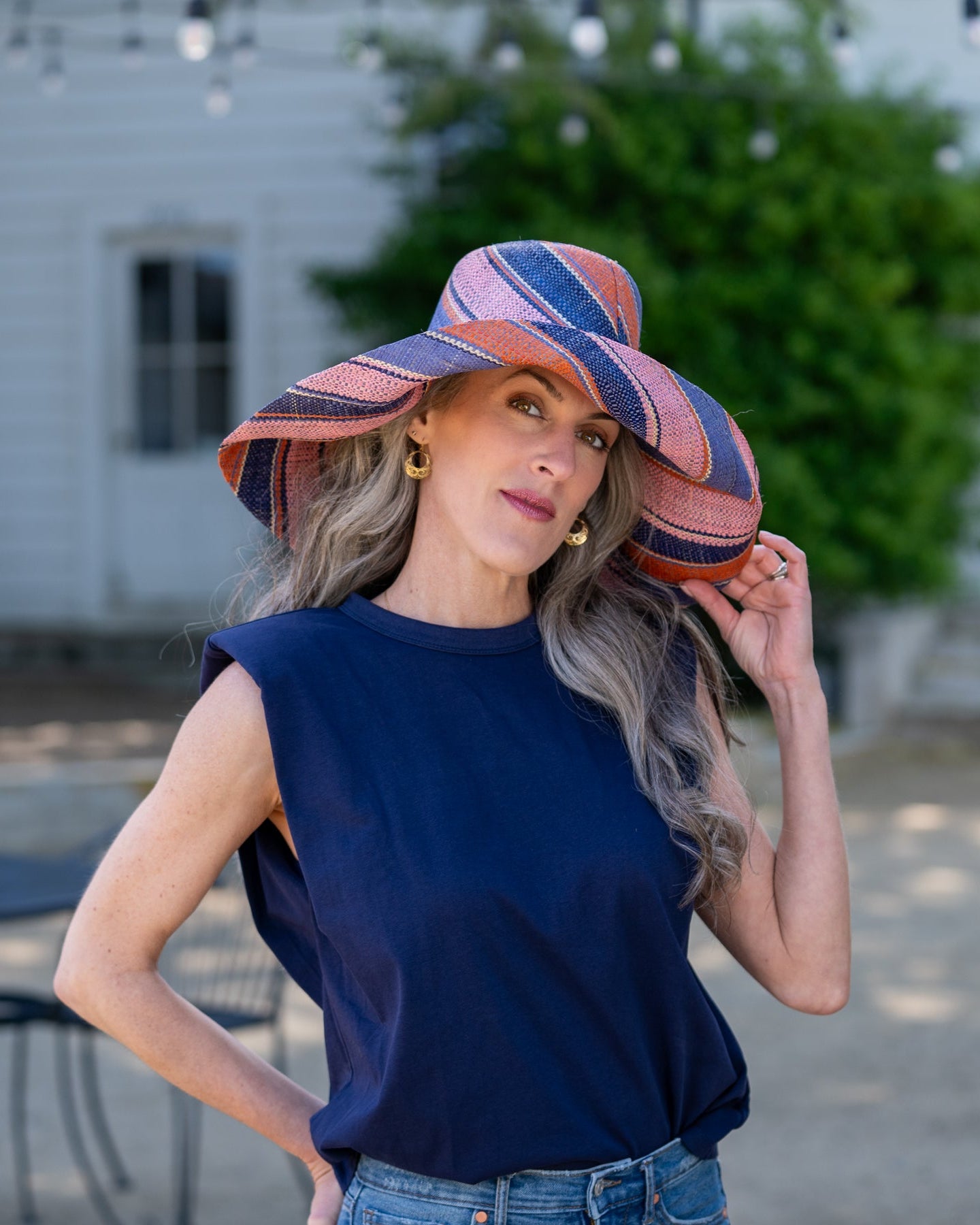 Model wearing Monica 7" Wide Brim Retro Swirl Packable Straw Sun Hat handmade loomed raffia in multi width stripes of denim retro/light/blue, coral orange/red, dusk navy/dark/blue, and light pink create a swirl pattern - Shebobo