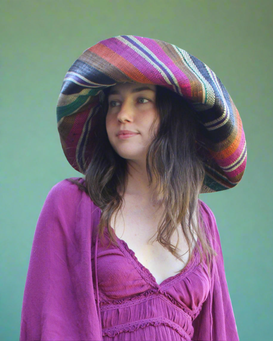 Model wearing Monica 7" Wide Brim Revel Swirl Multicolor Stripes Packable Straw Sun Hat Handmade loomed raffia in multi width bands of coral orange, fuchsia pink, teal blue/green, purple, cinnamon/tobacco/brown, black, natural straw color etc. create a swirl pattern - Shebobo