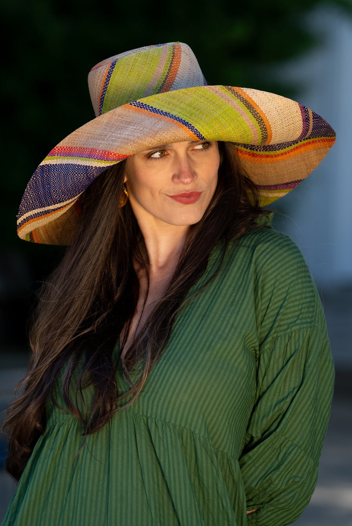 Model wearing Monica 7" Wide Brim Rio Swirl Multicolor Stripes Packable Straw Sun Hat Handmade loomed raffia in multi width bands of cappuccino light brown, lime green, saffron yellow, red, purple, navy blue, natural straw color, etc. create a swirl pattern - Shebobo