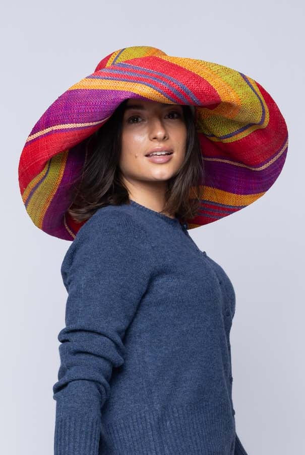 Model wearing Monica 5" & 7" Wide Brim Sangria Swirl Multicolor Stripes Packable Straw Sun Hat Handmade loomed raffia in multi width bands of red, purple, midori lime/green, turquoise blue, saffron yellow/orange, natural straw color, etc. create a swirl pattern - Shebobo