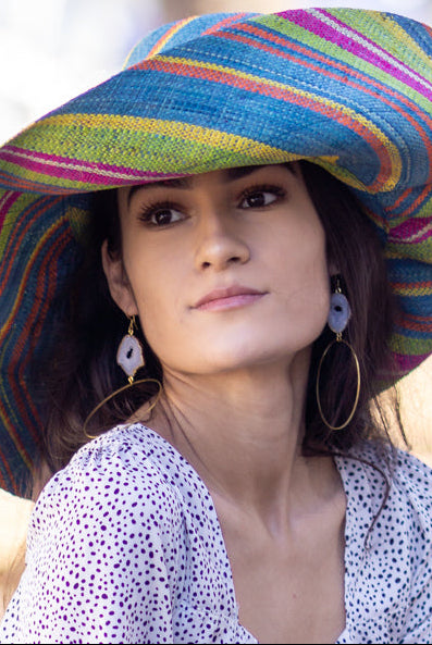Model wearing 7" Wide Brim Turquoise and Lime Multicolor Stripes Packable Straw Sun Hat Handmade loomed raffia multi width bands of turquoise blue, lime green, fuchsia pink, orange, yellow, and natural straw color create a swirl pattern - Shebobo