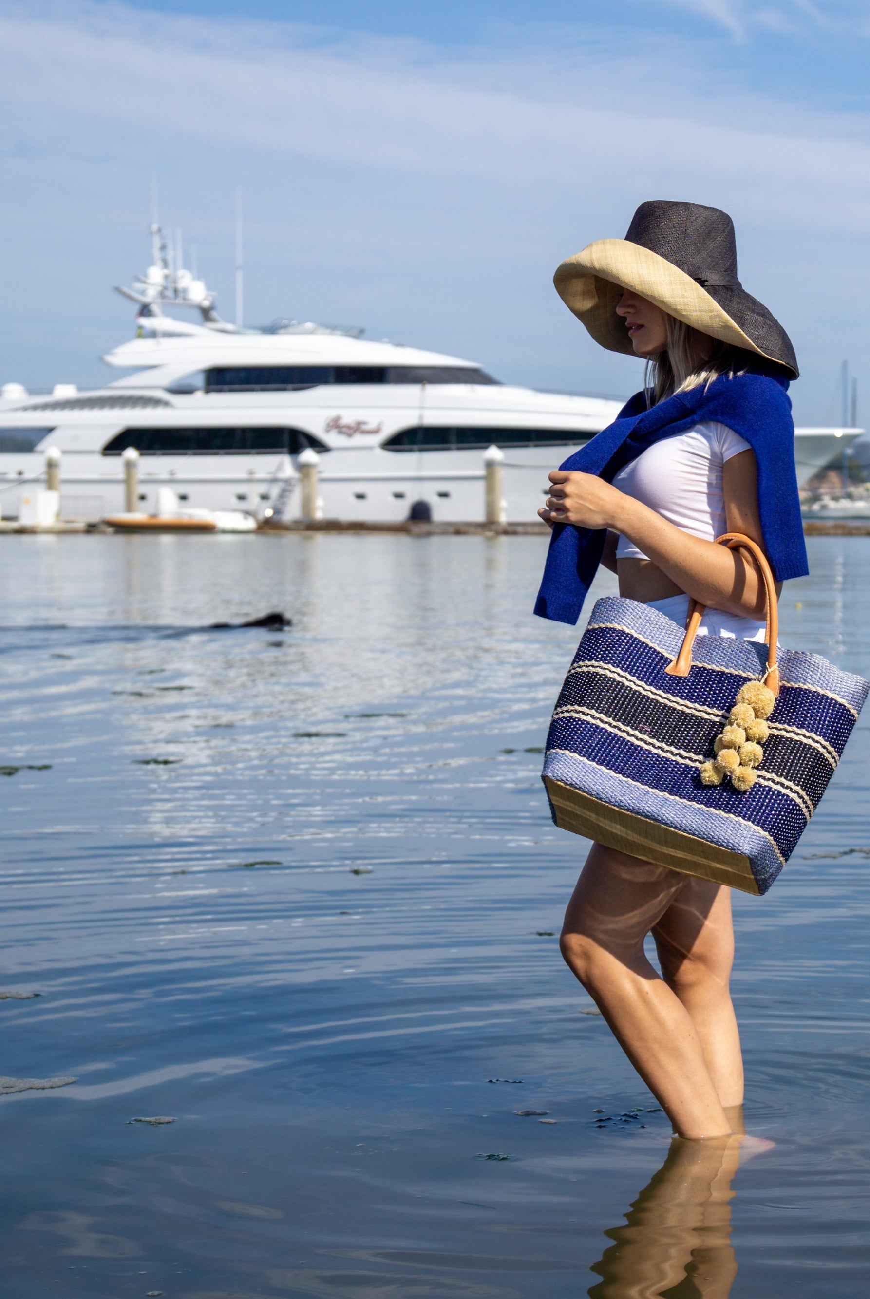 Model wearing Monica 7" Wide Brim Two Tone Black Packable Straw Sun Hat handmade loomed raffia color block pattern of the top half black and the bottom half natural straw color - Shebobo (with Cabrillo Blue Multi Stripe Sisal Basket Bag)