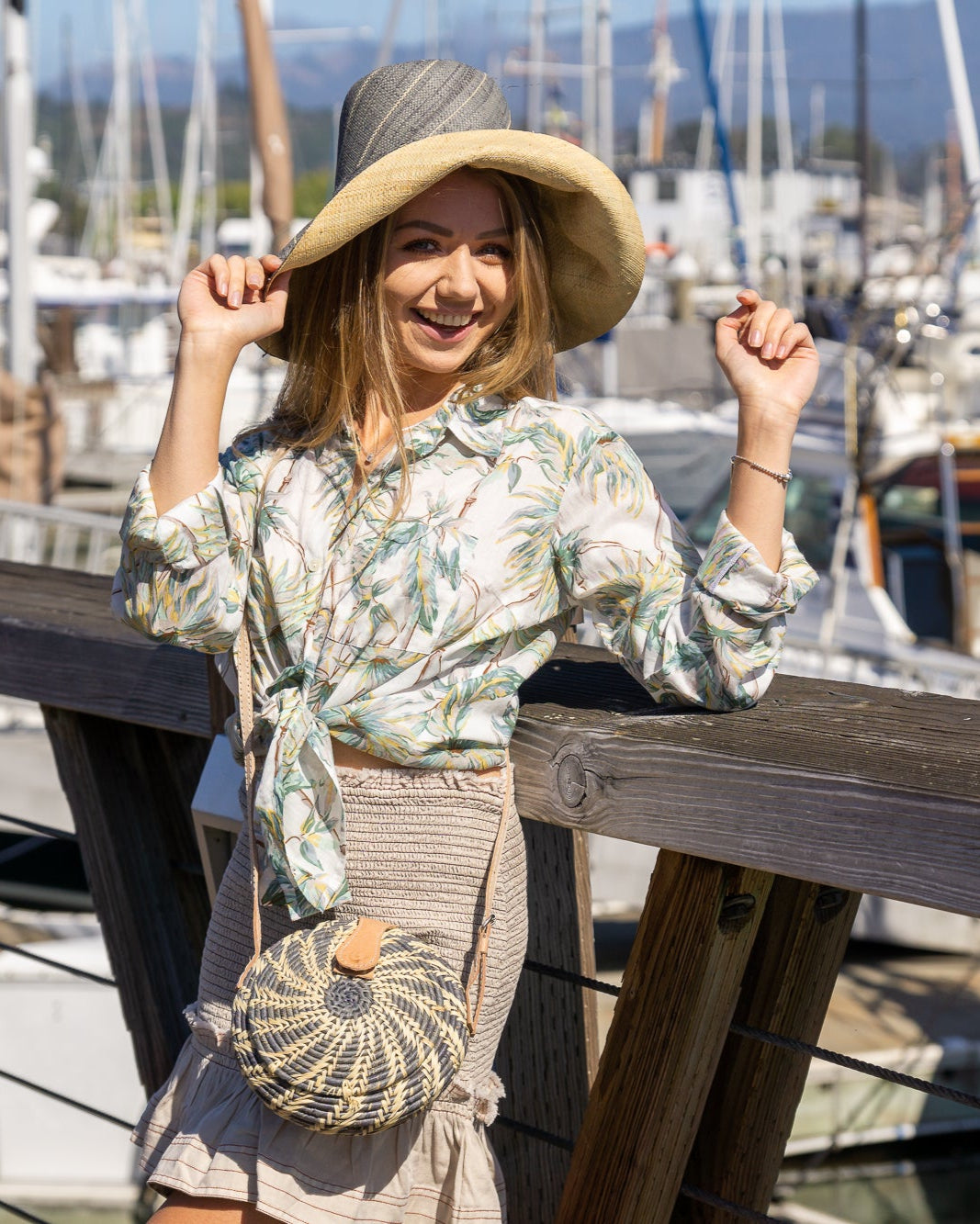Model wearing Monica 5" Wide Brim Two Tone Grey Pinstripes Packable Straw Sun Hat handmade loomed raffia color block pattern with the top half wide bands of grey with narrow bands of natural straw color creating a pinstripe swirl and the bottom half natural straw color - Shebobo (with Clamshell Grey Two Tone Straw Crossbody Bag Purse)
