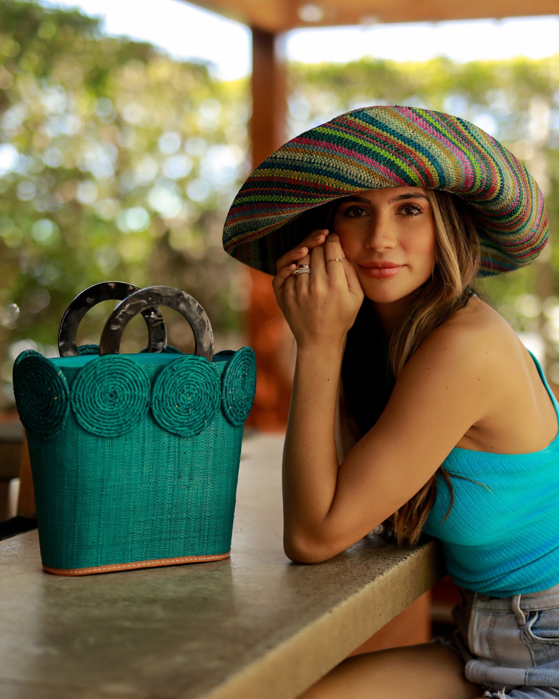 Model wearing Monica 5" Wide Brim Turquoise Stripes Multicolor Packable Straw Sun Hat Handmade loomed raffia in bands of natural, black, purple, yellow, orange, turquoise, grey, red, pink, and brown create a swirl pattern - Shebobo (with Tazi Turquoise Disc Straw Bucket Handbag)