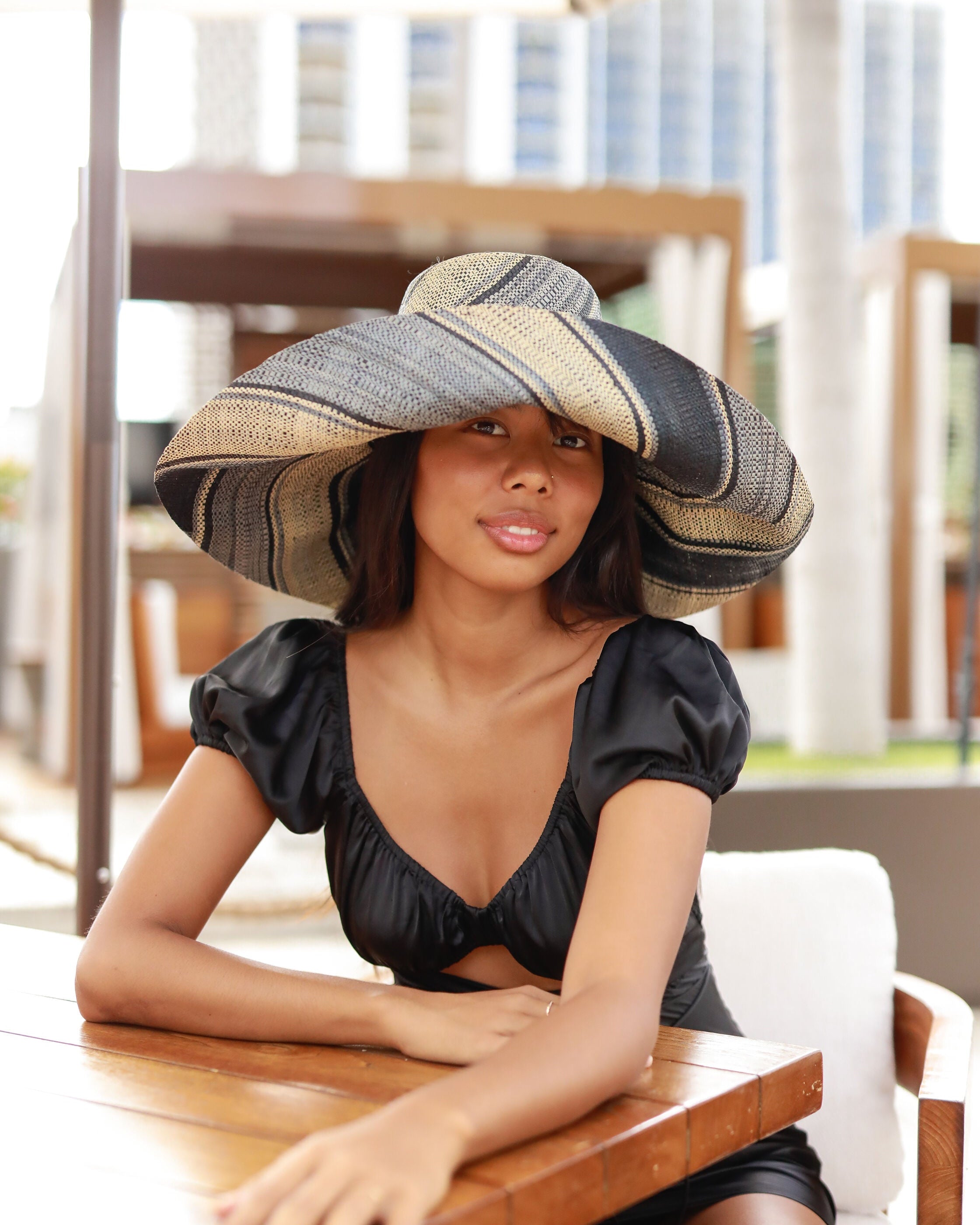 Model wearing Monica 7" Wide Brim Black Swirl Multicolor Stripe Pattern Packable Straw Sun Hat handmade loomed raffia in multi width bands of black, grey, and natural straw color create a striped swirl pattern - Shebobo