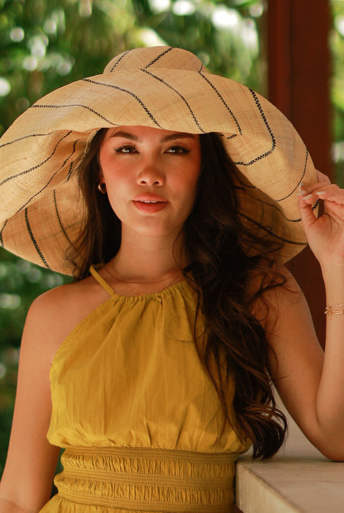 Model wearing Monica 7" wide brim natural and black pinstripes packable raffia straw hat handmade loomed raffia in wide bands of natural straw color with black narrow bands create a stripe swirl pattern - Shebobo