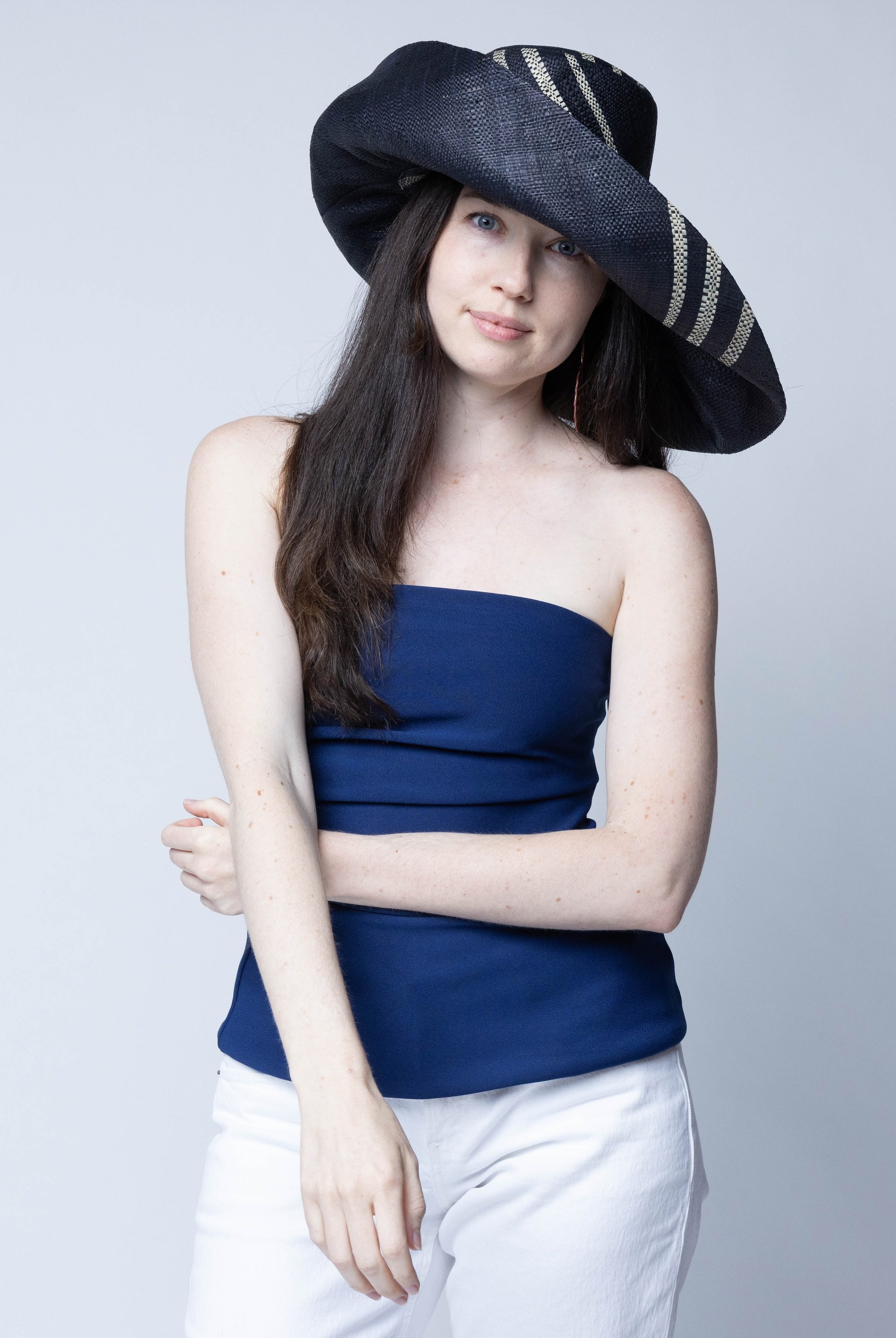 Model wearing Monica 7" Wide Brim Racing Stripe Packable Straw Sun Hats handmade loomed natural raffia palm fiber in a solid hue of black with a three stripe racing stripe pinstripe pattern of natural straw color that creates a swirl around the crown and brim of the hat lightweight breathable sun protection - Shebobo