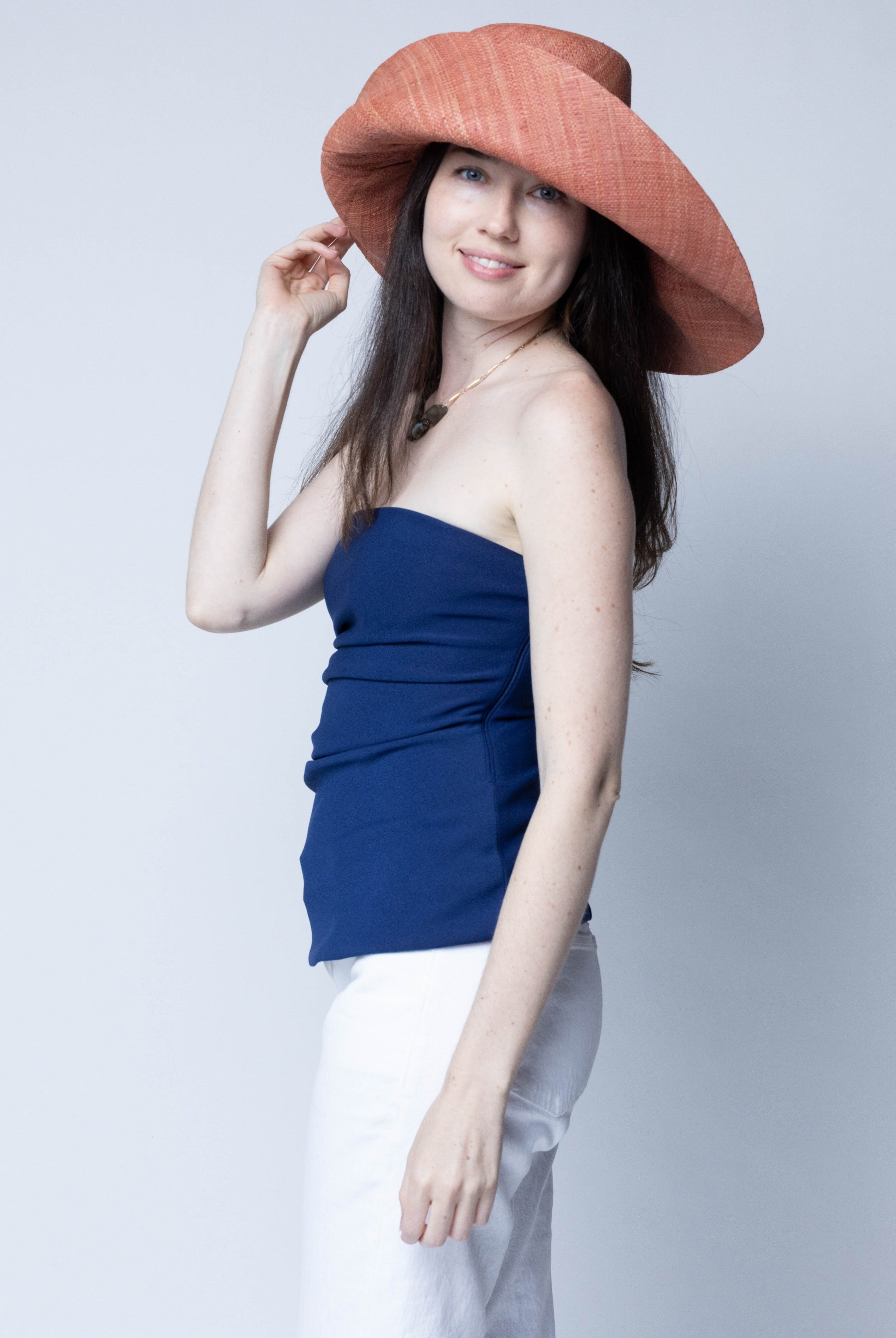 Model wearing Monica 7" Wide Brim Solid Color Packable Straw Sun Hat handmade loomed raffia in a solid hue of Blush orange/terracotta/pink - Shebobo