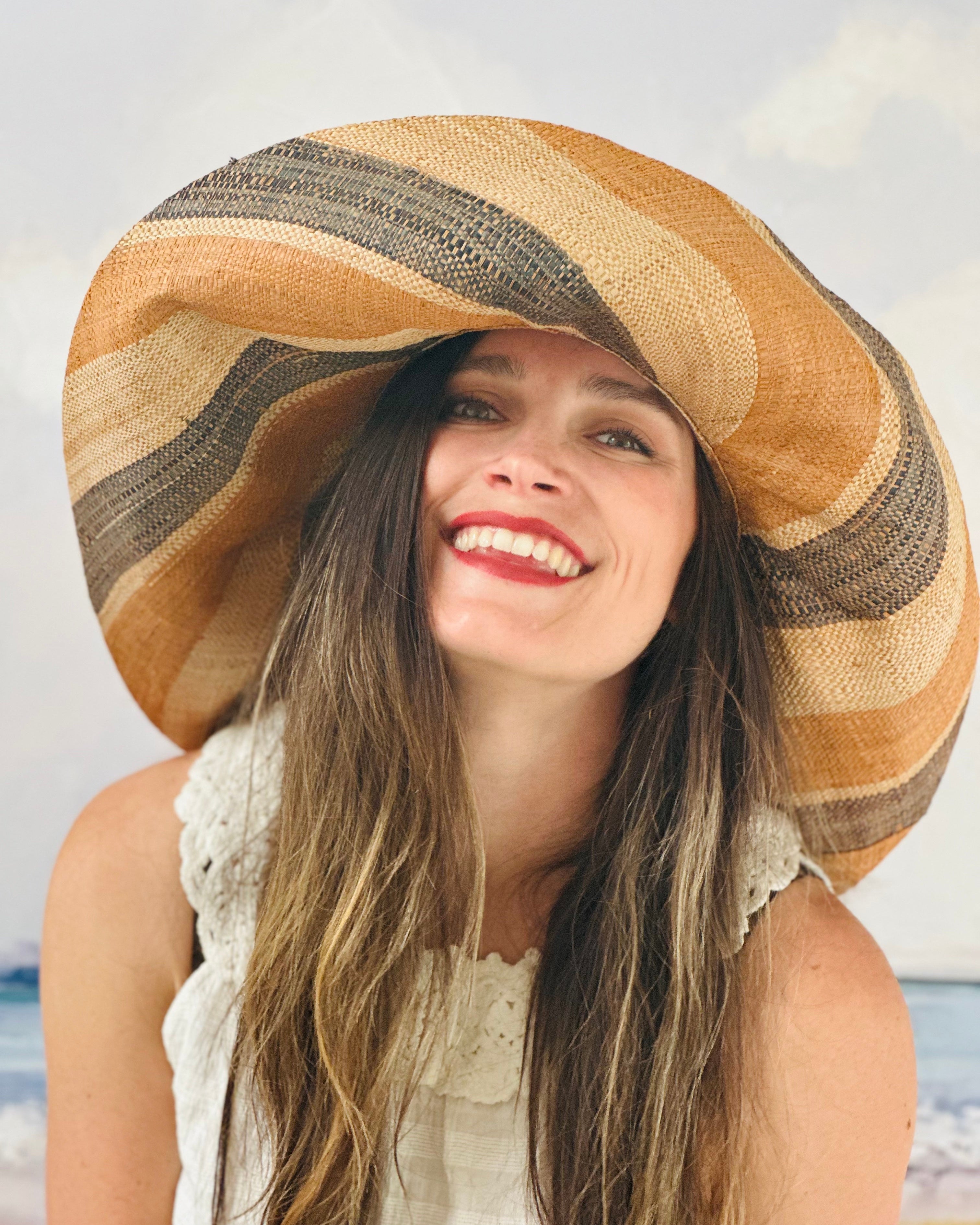 Model wearing Monica 7" Wide Brim Blush Swirl Multicolor Stripes Packable Straw Sun Hat Handmade loomed raffia in multi width bands of blush orange/pink, grey, and natural create a swirl pattern - Shebobo