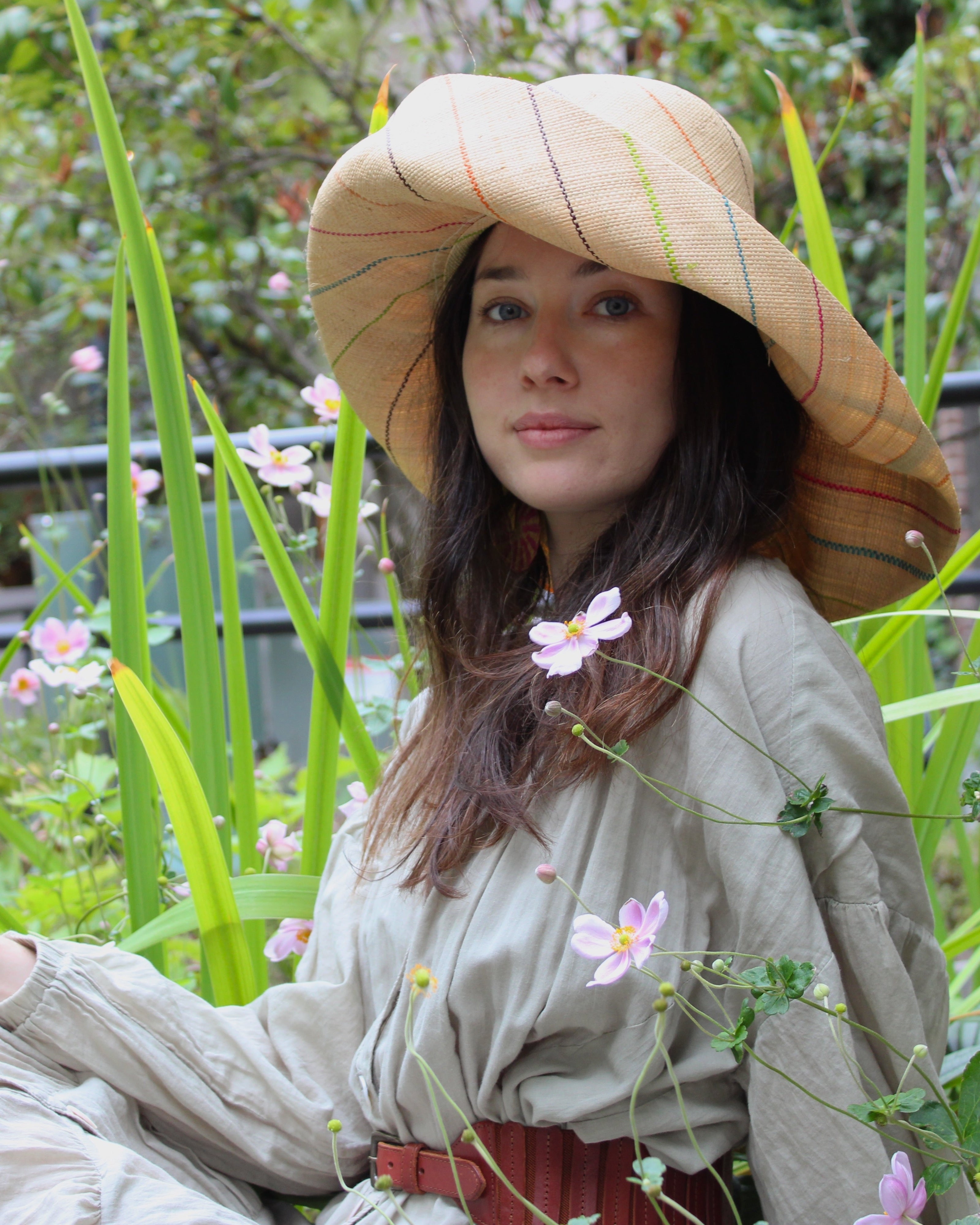 Model wearing Monica 7" wide brim natural and multicolor pinstripes packable raffia straw hat handmade loomed raffia in wide bands of natural straw color with narrow bands of lime green, bordeaux red, fuchsia pink, orange, cinnaon/tobacco/brown, blush orange/pink, etc. create a stripe swirl pattern - Shebobo