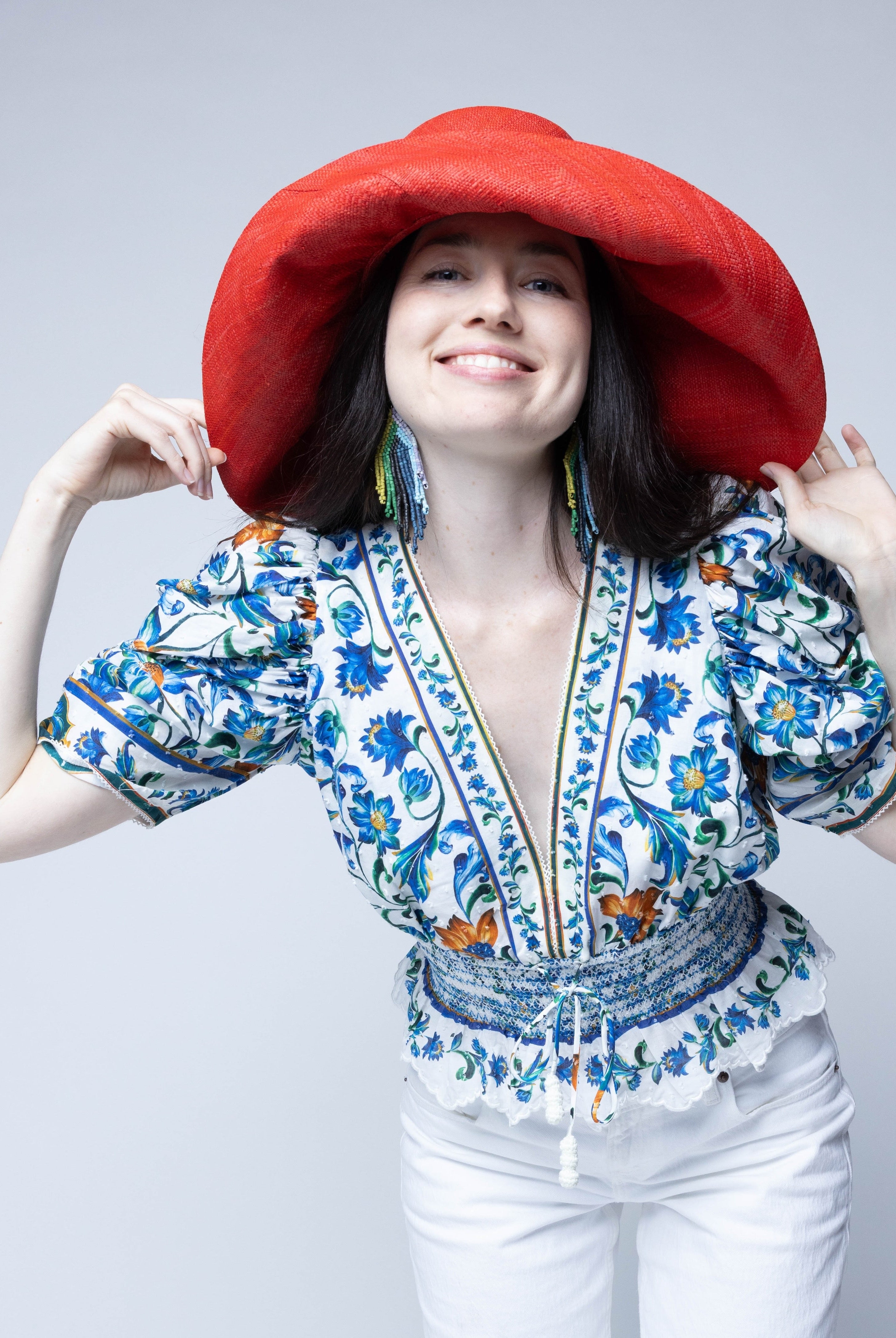 Model wearing Monica 7" Wide Brim Coral Solid Color Packable Straw Sun Hat handmade loomed raffia in a solid hue of coral orange/red - Shebobo