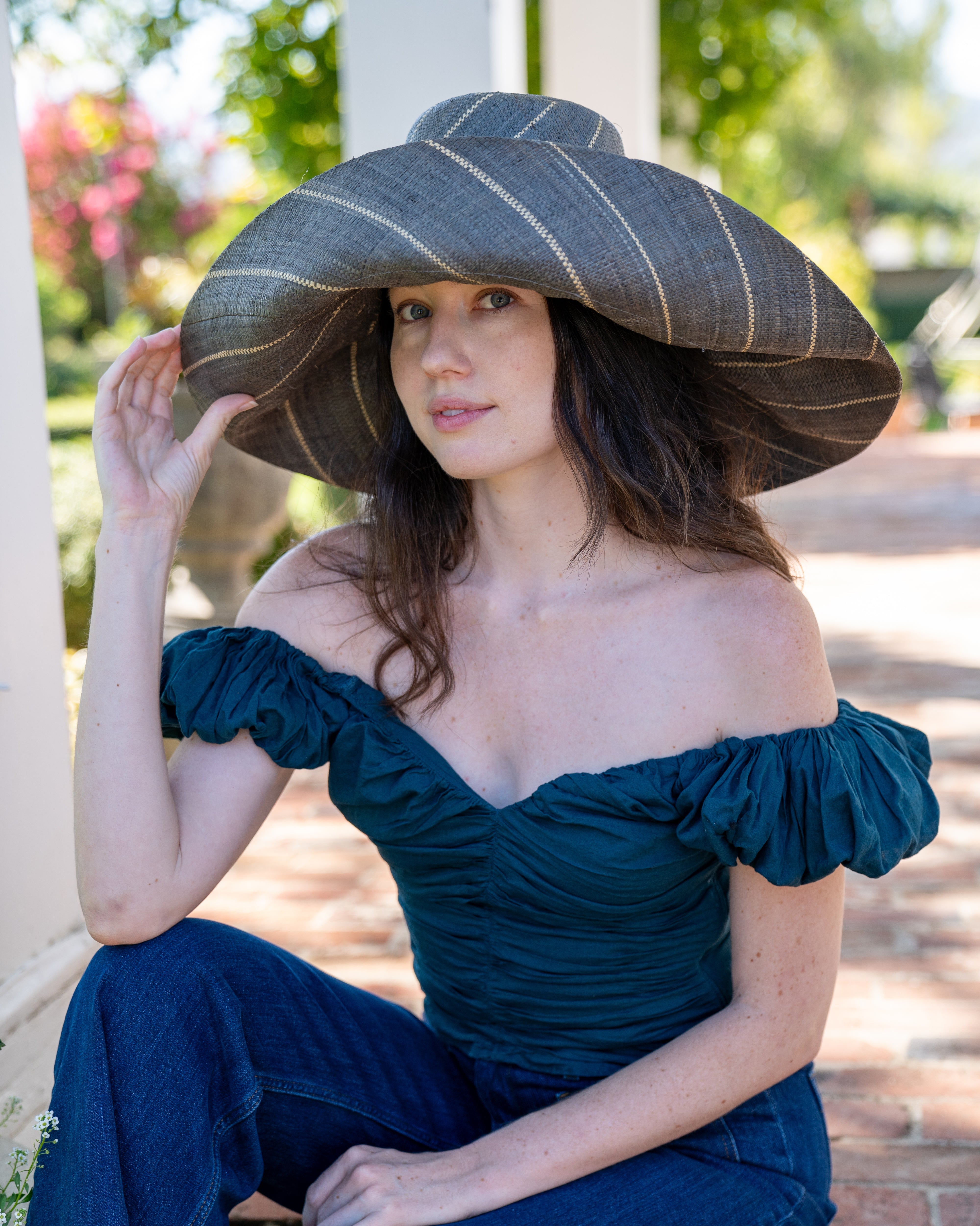 Model wearing Monica 7" Wide Brim Grey Pinstripes Packable Straw Sun Hat handmade loomed raffia in wide bands of grey with narrow bands of natural straw color create a striped swirl pattern - Shebobo