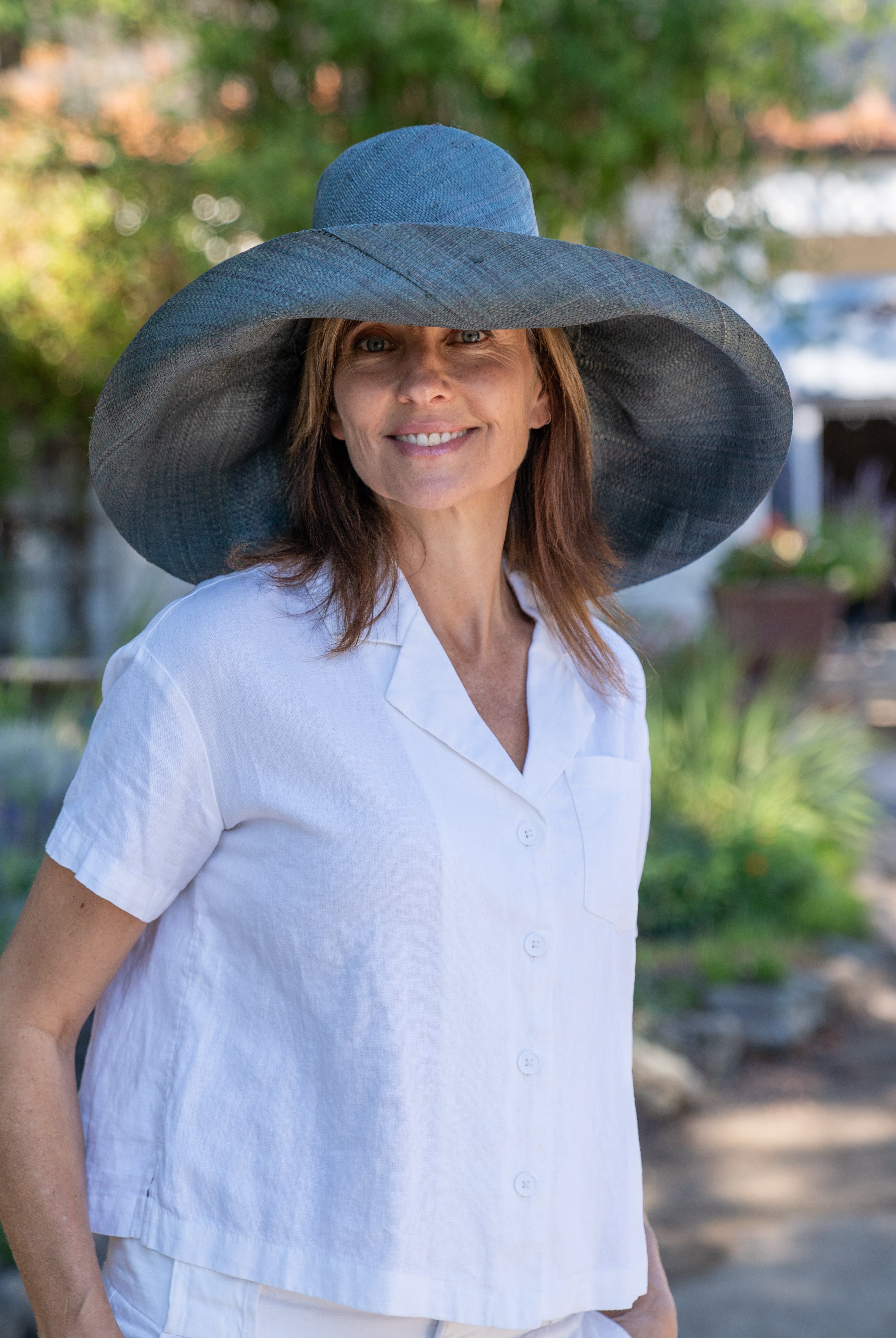 Model wearing Monica 7" Wide Brim Sea Sage Packable Straw Sun Hat handmade loomed raffia in a solid hue of blue/green/dark grey lightweight malleable flexible sun protection hat - Shebobo