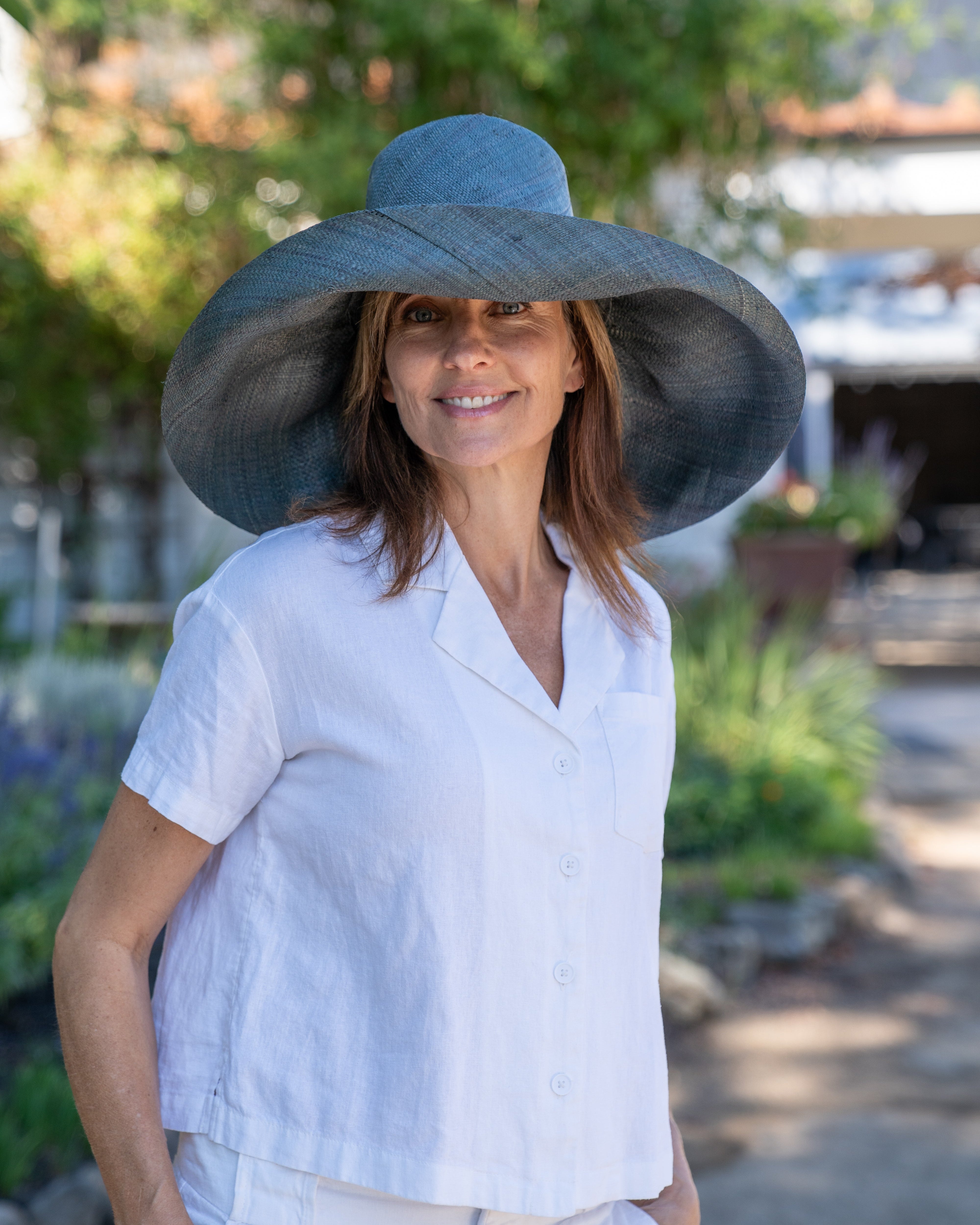 Model wearing Monica 7" Wide Brim Sea Sage Packable Straw Sun Hat handmade loomed raffia in a solid hue of blue/green/dark grey lightweight malleable flexible sun protection hat - Shebobo