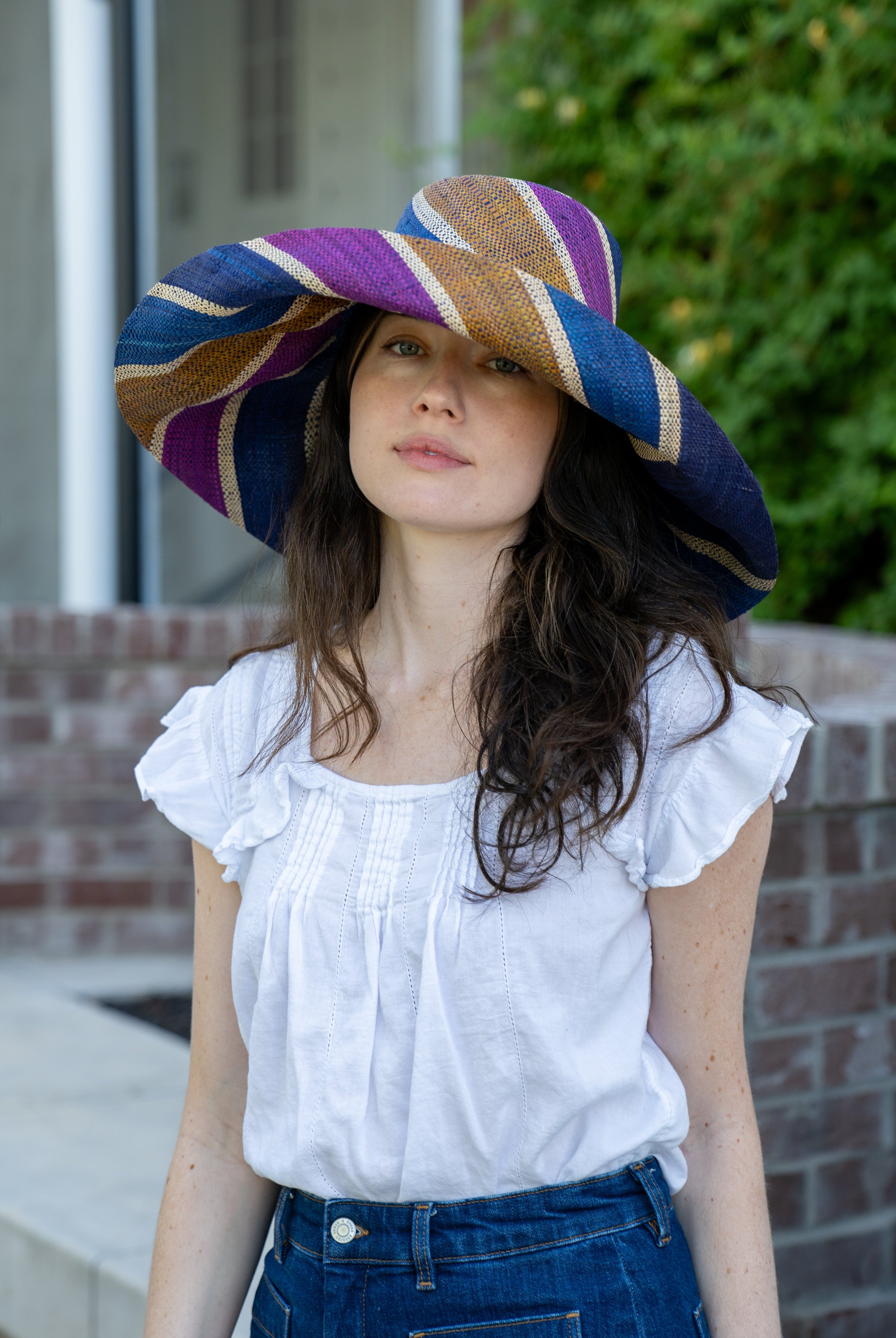 Model wearing Monica 7" Wide Brim Olive and Purple Swirl Multicolor Stripes Packable Straw Sun Hat Handmade loomed raffia multi width bands of turquoise blue, olive green, purple, and natural straw color create a swirl pattern - Shebobo