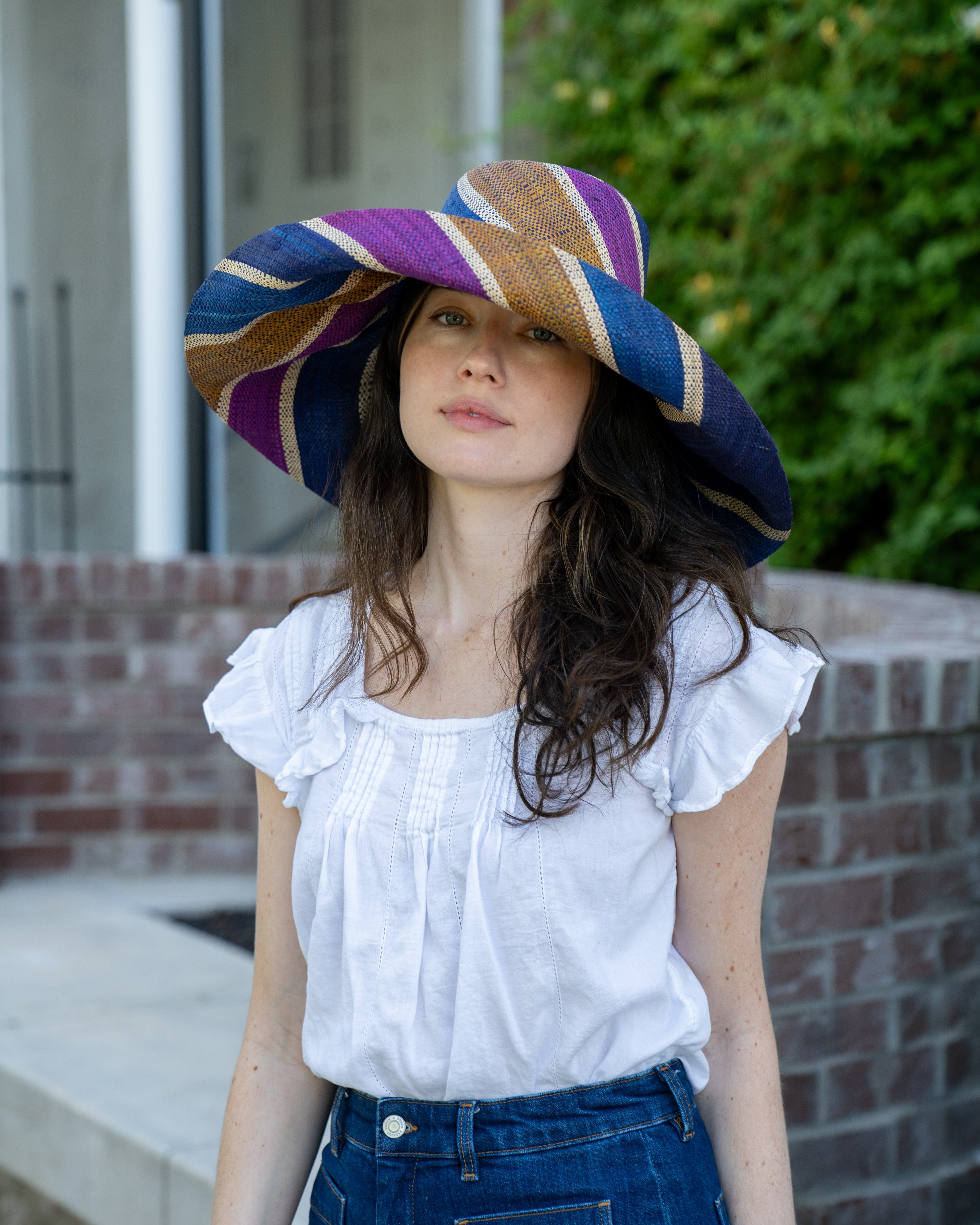 Model wearing Monica 7" Wide Brim Olive and Purple Swirl Multicolor Stripes Packable Straw Sun Hat Handmade loomed raffia multi width bands of turquoise blue, olive green, purple, and natural straw color create a swirl pattern - Shebobo