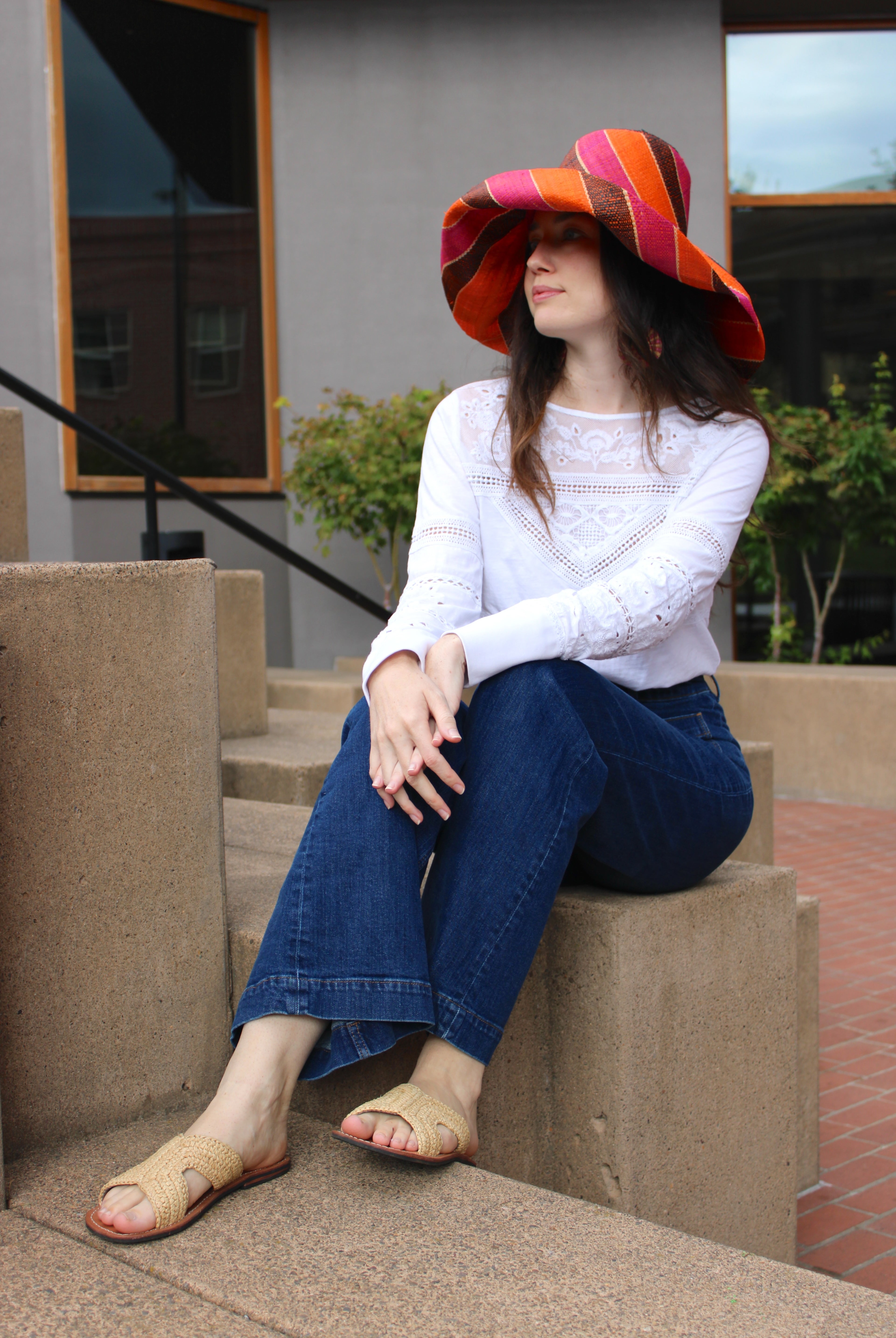 Model wearing Monica 7" Wide Brim Whimsy Swirl Multicolor Stripes Packable Straw Sun Hat Handmade loomed raffia in multi width bands of coral orange, fuchsia pink, black, natural straw color, etc. create a swirl pattern - Shebobo (with Lizzie Crochet Straw & Leather Sandal Shoes)