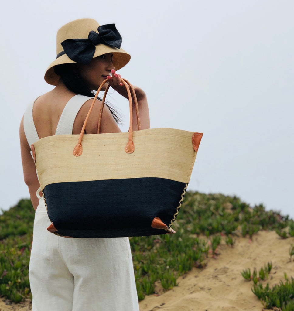 Model wearing Monterey Two Tone Straw Tote Bag handmade loomed raffia fibers in a color block pattern of natural straw colored upper half, and black lower half - Shebobo