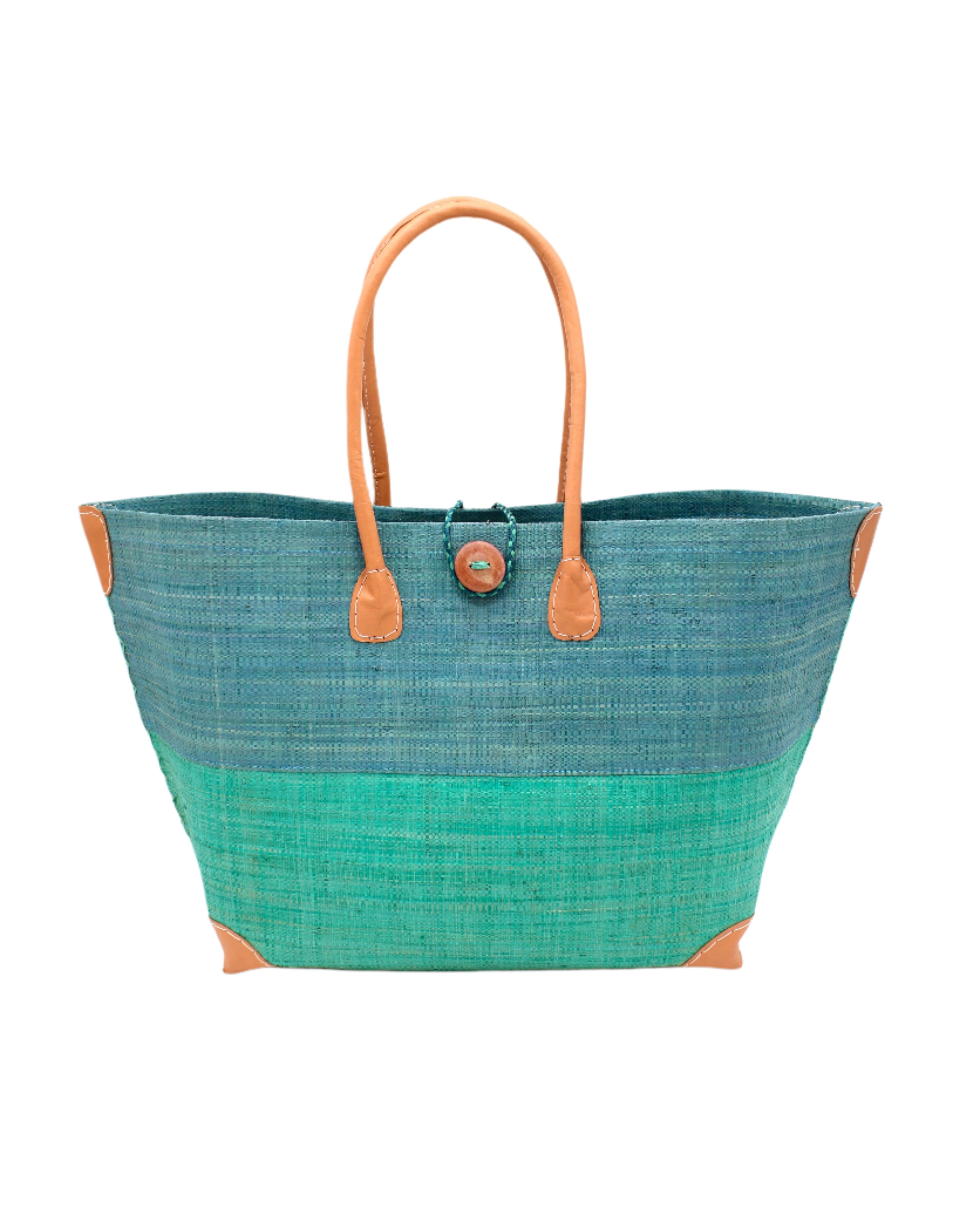 Model wearing Monterey Two Tone Straw Tote Bag handmade loomed raffia fibers in a color block pattern of turquoise blue colored upper half, and seafoam blue/green lower half - Shebobo