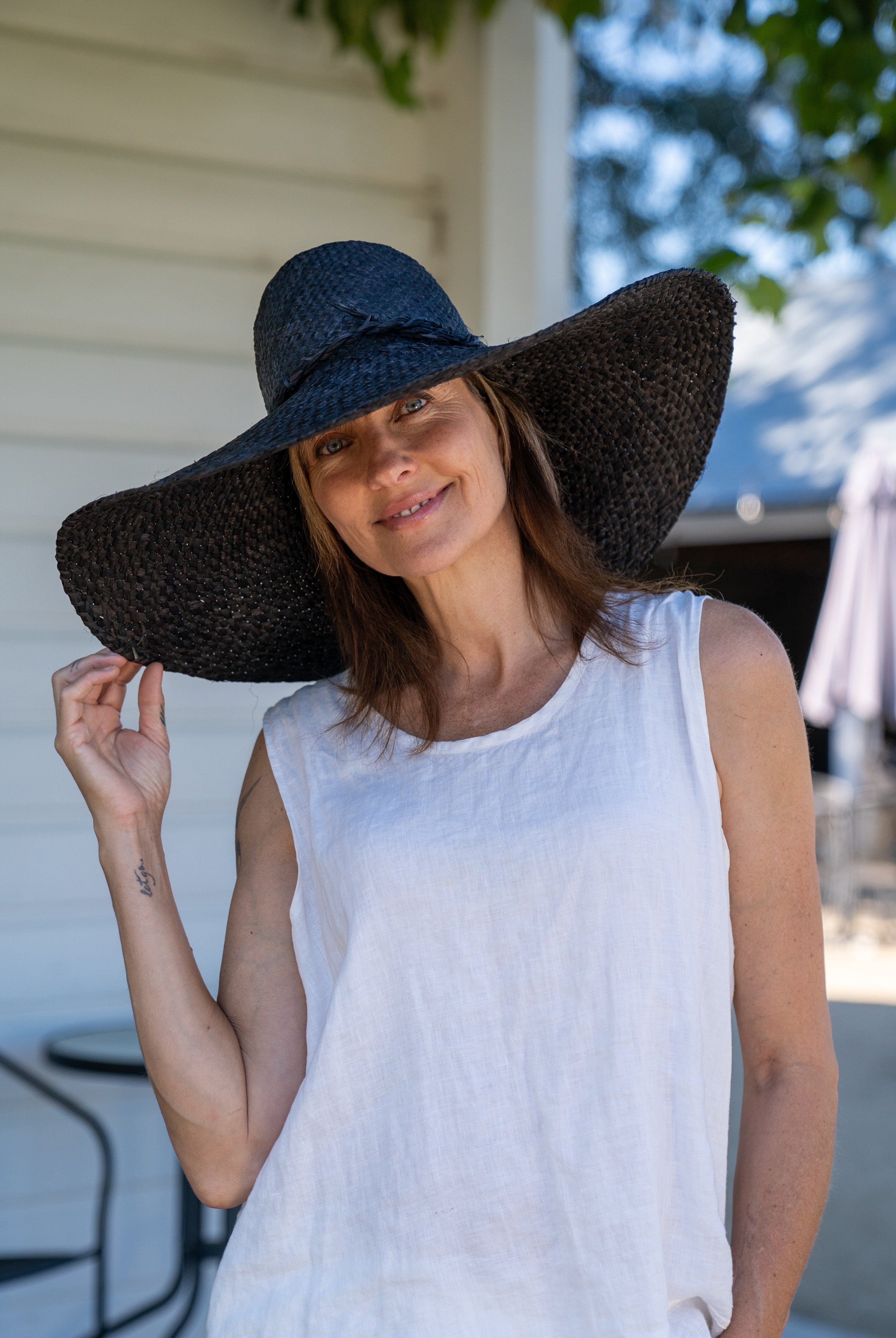 Model wearing 7" Wide Brim Natasha Black Woven XL Straw Sun Hat handmade woven natural raffia palm fiber in a solid hue of black with matching adjustable twisted raffia hat band and and extra wide brim - Shebobo