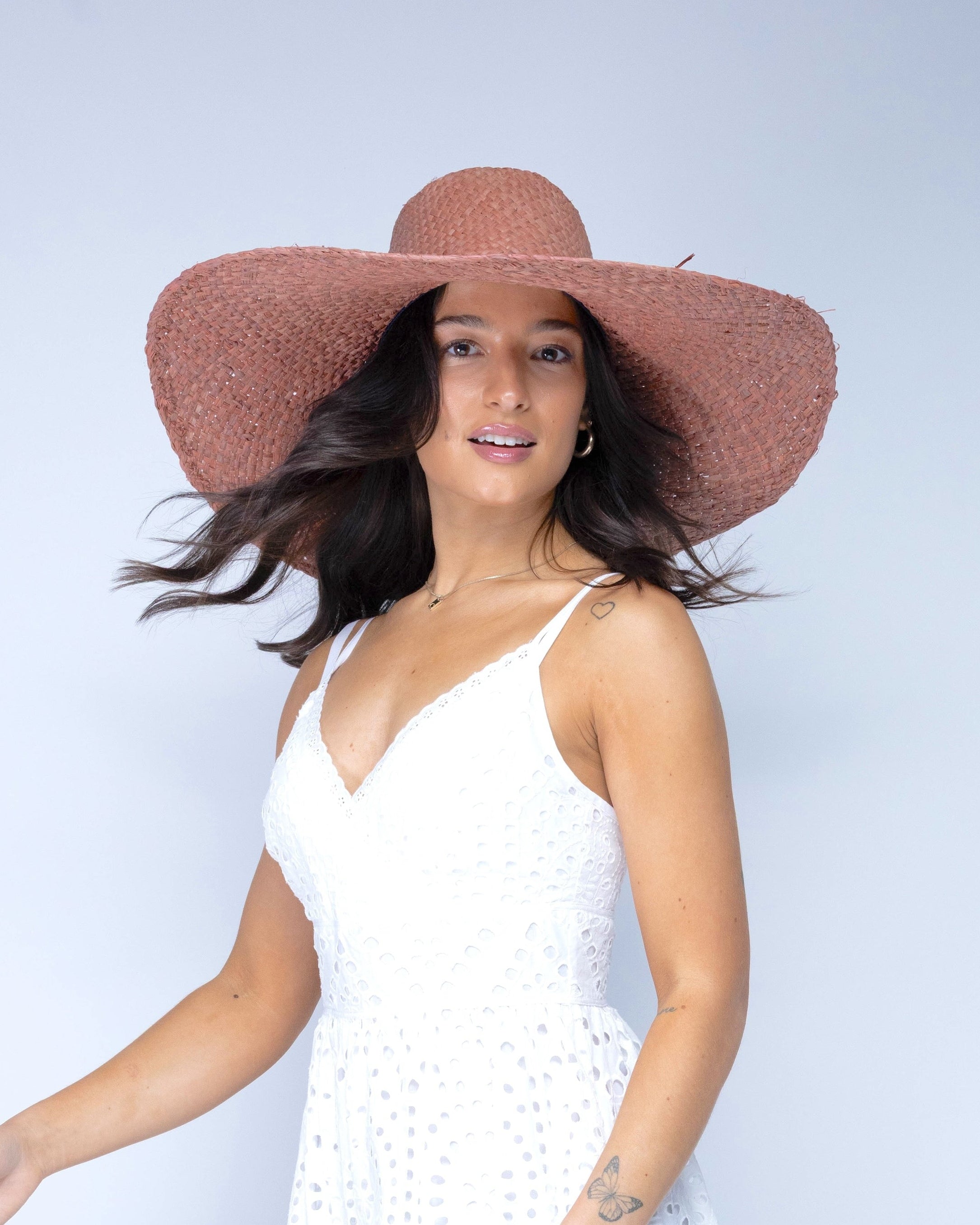 Model wearing 7" Brim Natasha Blush Woven XL Straw Sun Hat handmade woven natural raffia palm fiber in a solid hue of blush red/pink with matching adjustable twisted raffia hat band and and extra wide brim - Shebobo
