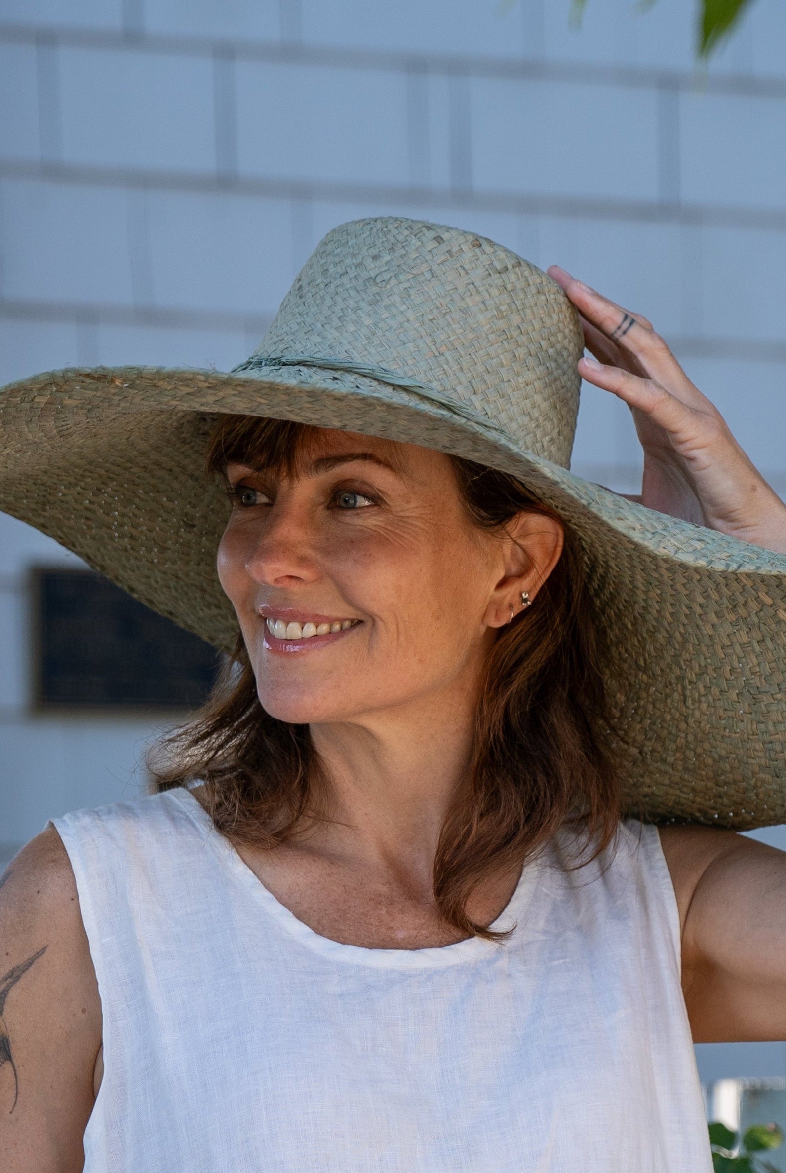 Model wearing 7" Wide Brim Natasha Ocean Mist Woven XL Straw Sun Hat handmade woven natural raffia palm fiber in a solid hue of ocean mist sage/green with matching adjustable twisted raffia hat band and and extra wide brim - Shebobo