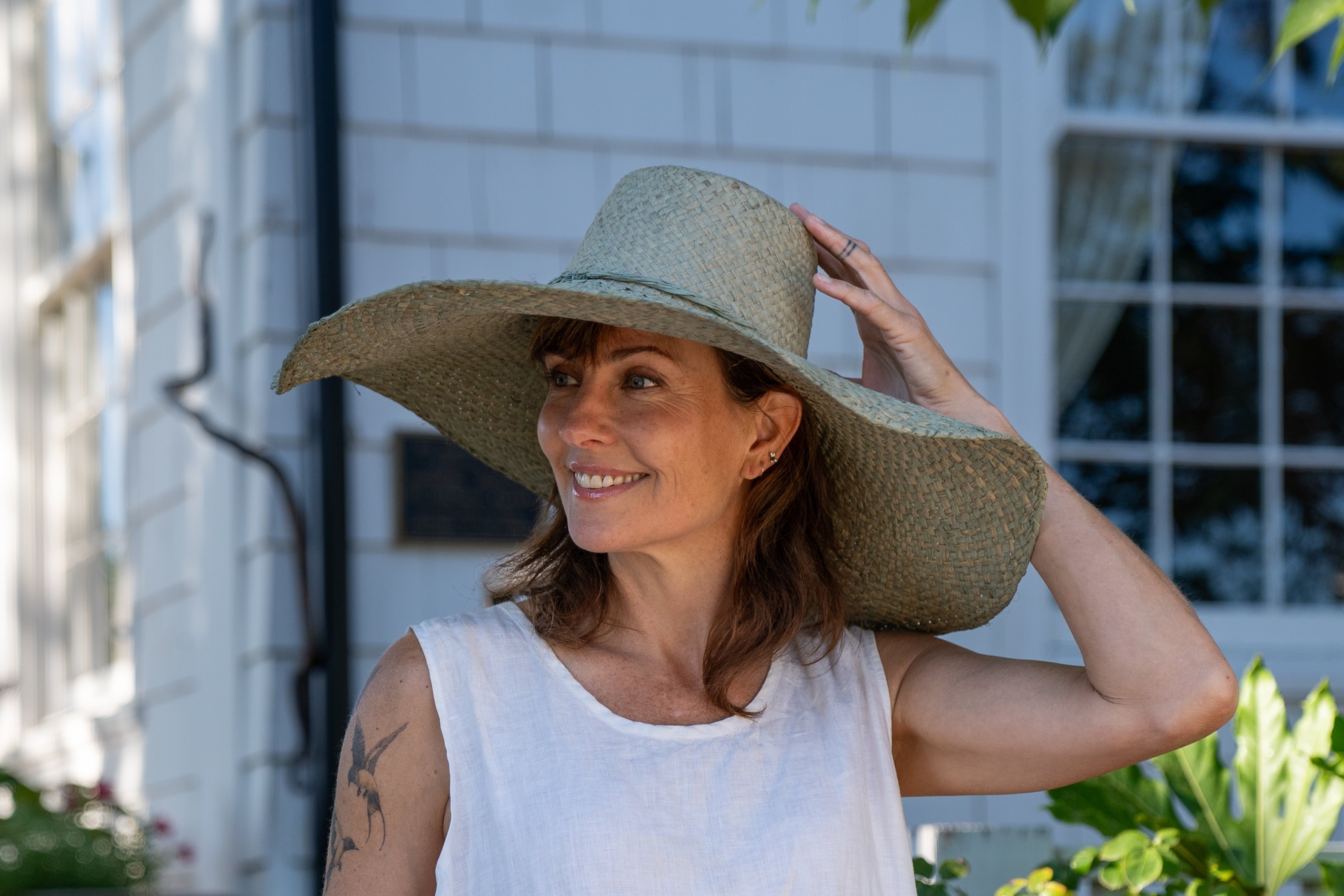 Model wearing 7" Wide Brim Natasha Ocean Mist Woven XL Straw Sun Hat handmade woven natural raffia palm fiber in a solid hue of ocean mist sage/green with matching adjustable twisted raffia hat band and and extra wide brim - Shebobo
