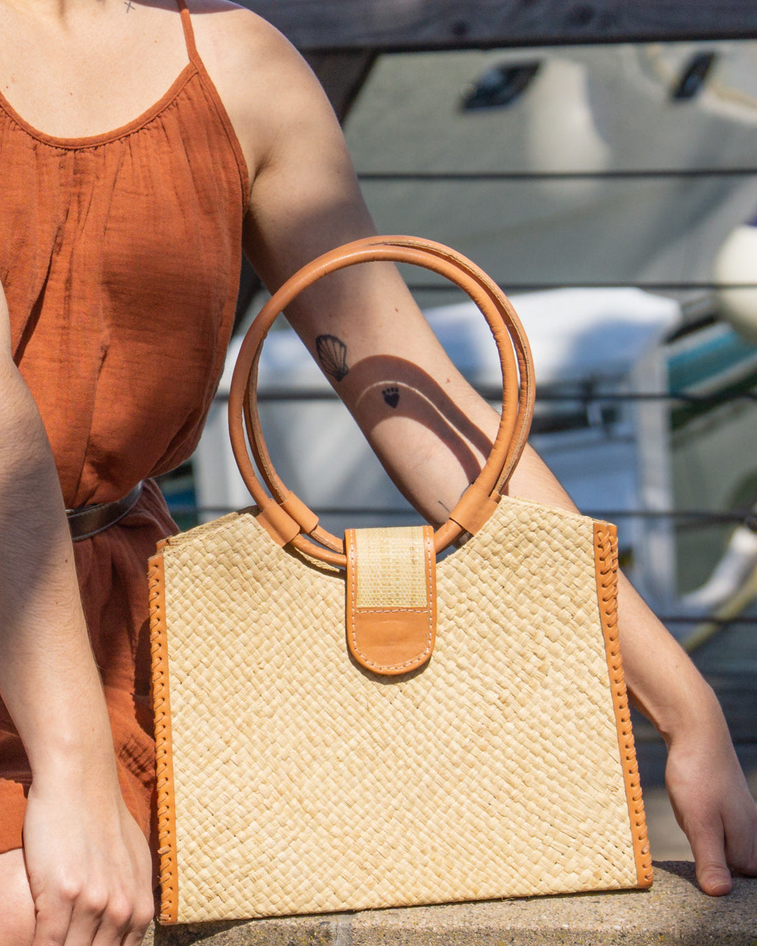 Model wearing Ibiza Natural Straw HandBag with Leather Handles handmade woven natural raffia fiber purse with crosshatch pattern and loomed sides with leather loop handles, woven leather side seam binding, and flap closure - Shebobo