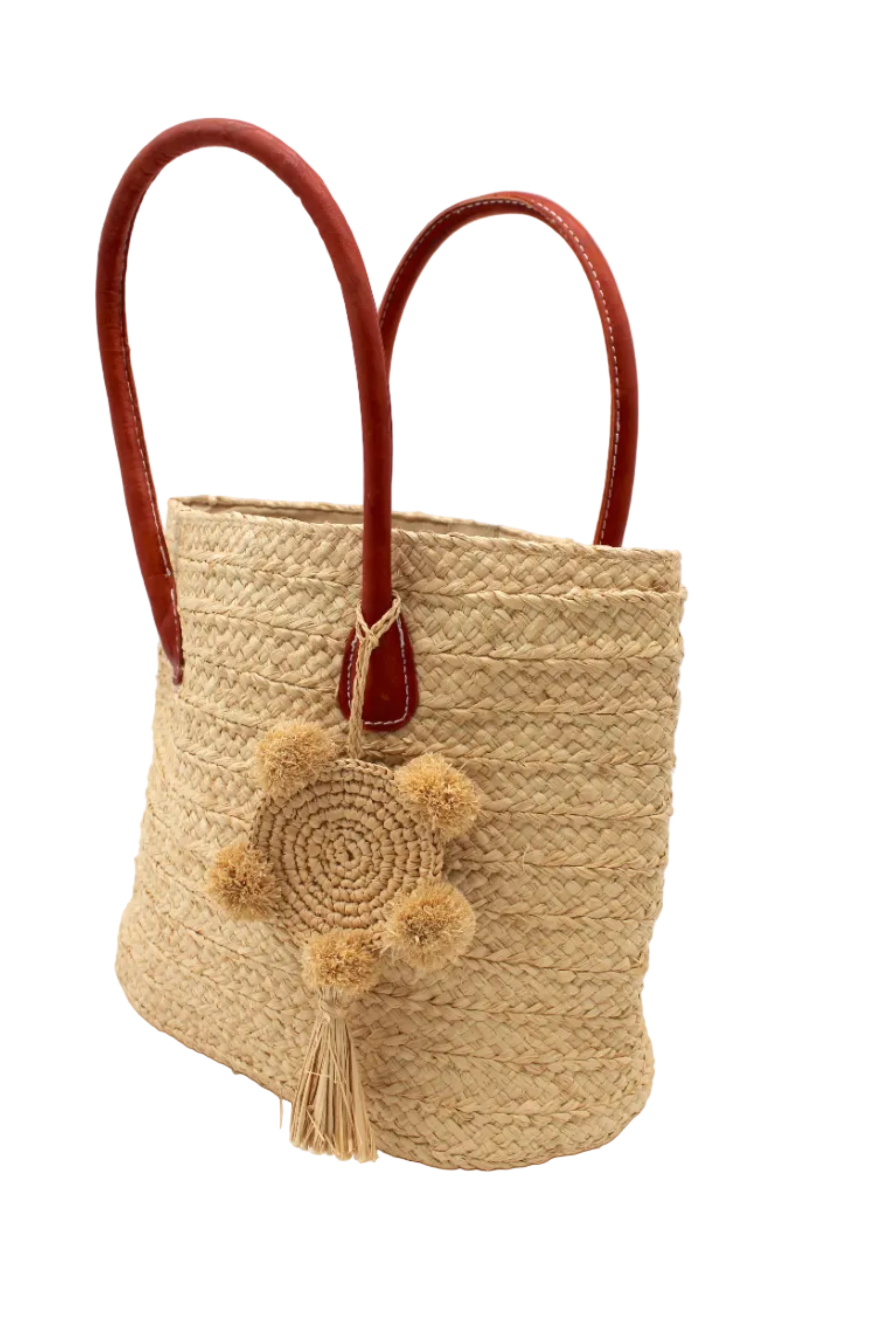 Side view Nomena Braided Straw Basket Handbag handmade braided natural raffia palm fiber in a solid hue of natural straw color woven into concentric horizontal bands of subtle texture spiraling around the bag with leather handles beach bag shoulder bag purse with matching crochet dreamcatcher pompom and tassel charm embellishment - Shebobo