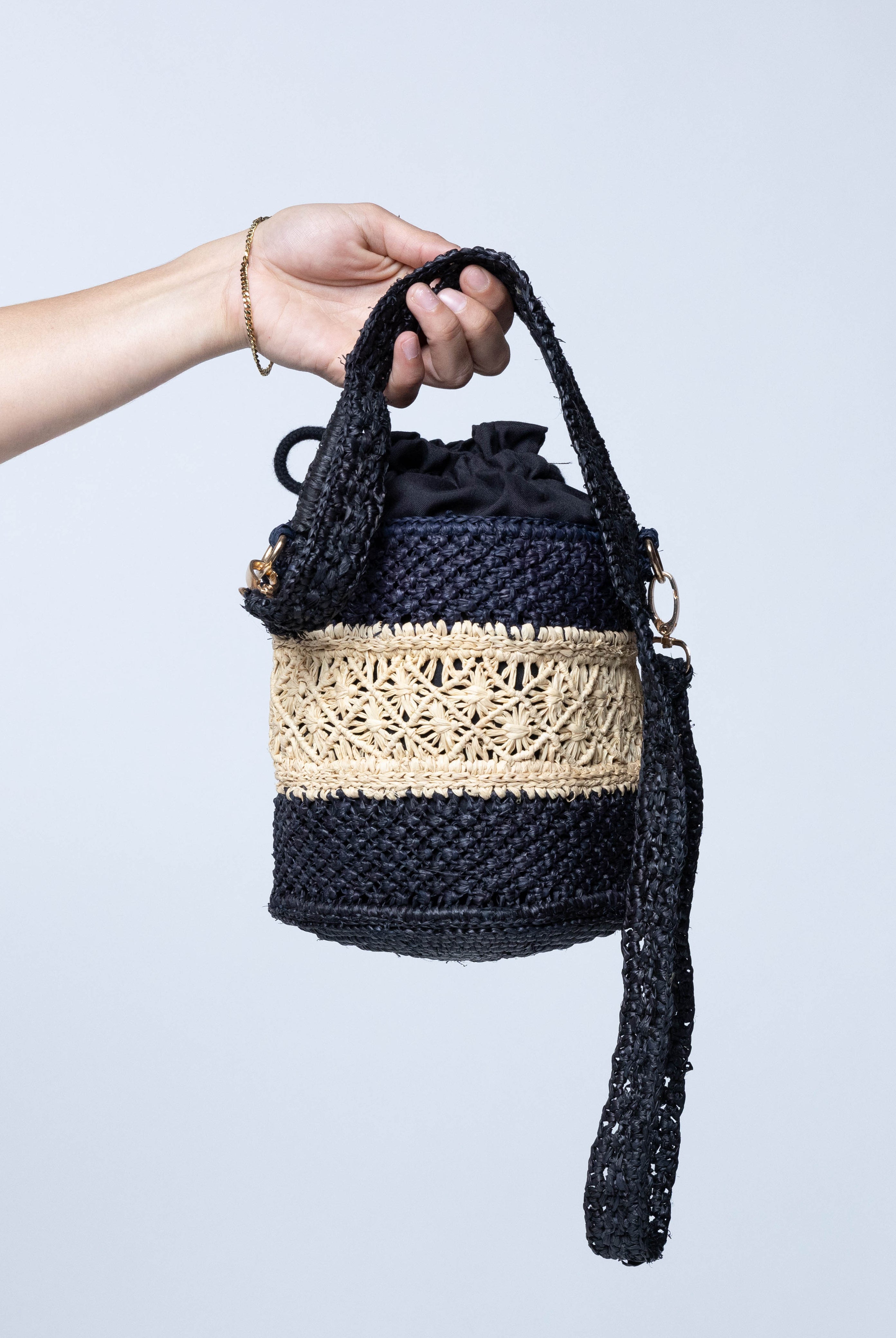 Model wearing Paloma Macrame Diamond & Crochet Straw Bucket Handbag Convertible Crossbody Bag handmade natural raffia palm fiber macrame and crochet in a two tone multicolor of a diamond pattern horizontal band in the center of natural straw color centered with black around the bottom and top of the round bottomed bag in a subtle link crochet texture with detachable shoulder strap - Shebobo