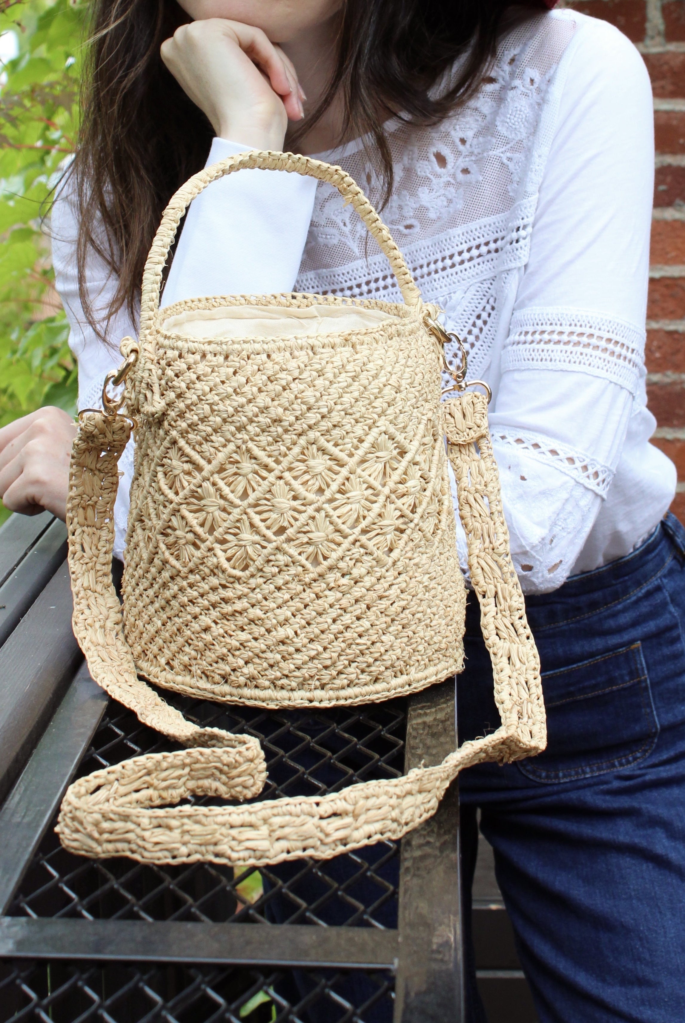 Model wearing Paloma Macrame Diamond & Crochet Straw Bucket Handbag Convertible Crossbody Bag handmade natural raffia palm fiber macrame and crochet in a solid hue of natural straw color round bottomed bag with three even horizontal bands of texture the top and bottom subtle link pattern and the center geometric diagonal starburst or flower in diamond pattern with detachable shoulder strap - Shebobo