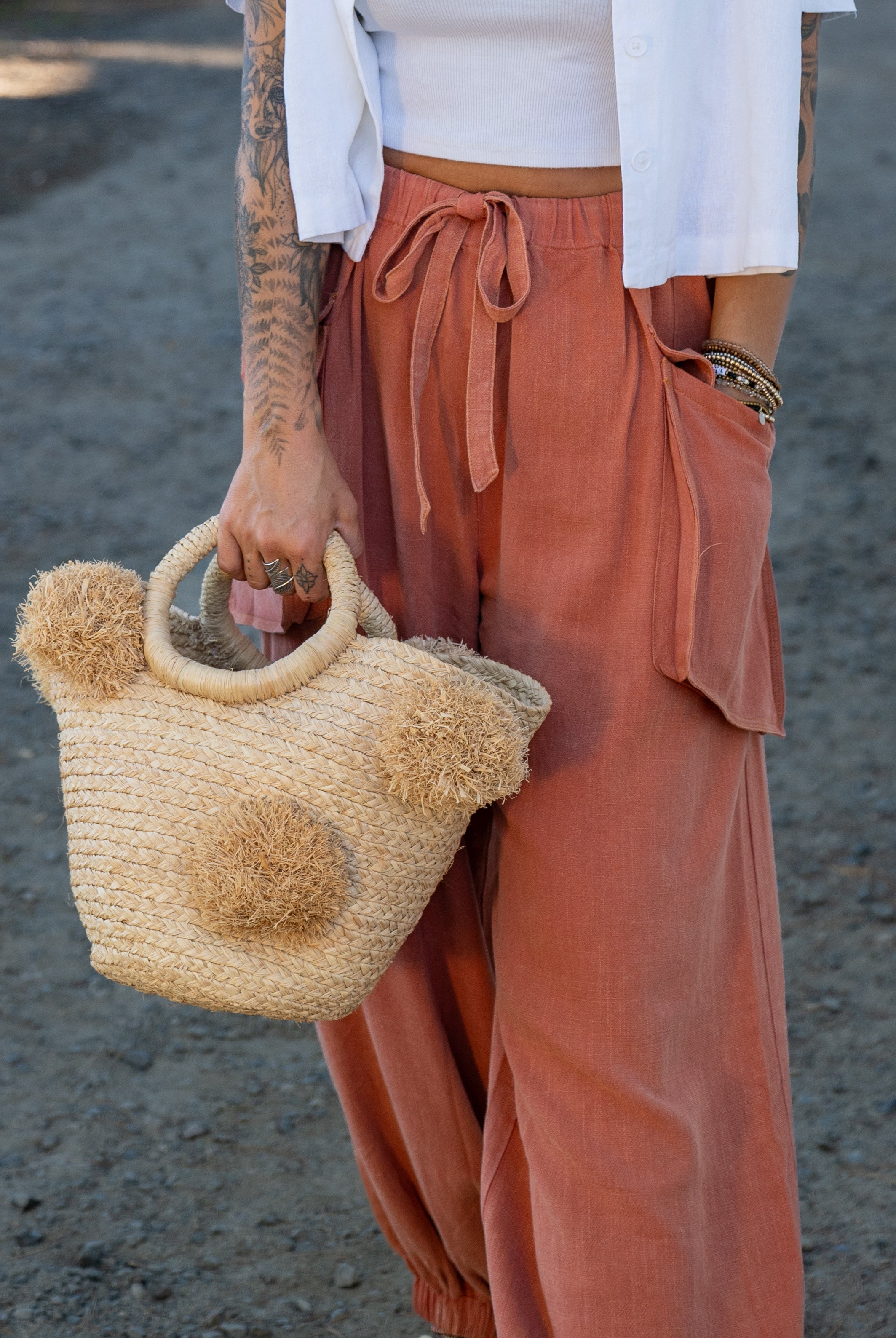 Model wearing Phi Phi Natural Braided Straw Basket with Oversized Raffia Poufs handmade raffia palm fiber braided into a solid hue of natural straw color with three randomly placed matching hand-brushed fringe poufs per side for embellishment with loop wrap top edging and crochet loop/braided handles bag handbag - Shebobo