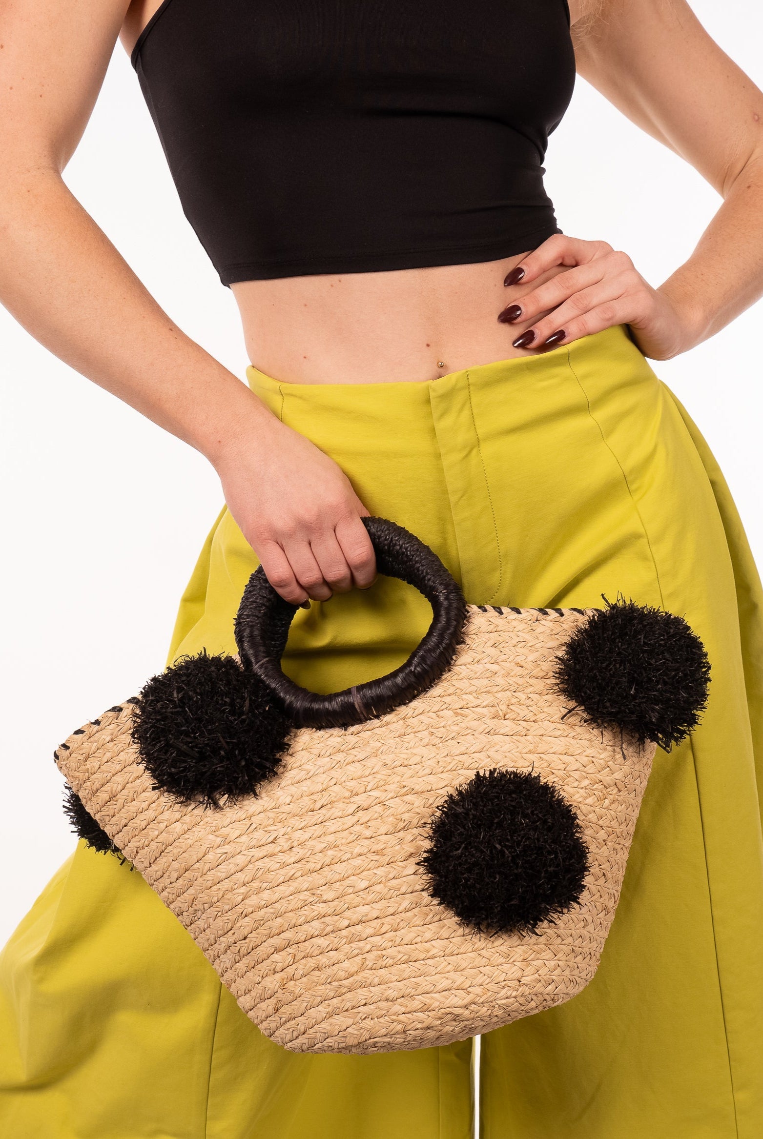Model wearing Phi Phi Black and Natural Braided Straw Basket with Oversized Raffia Poufs handmade raffia palm fiber braided into a solid hue of natural straw color with three randomly placed black hand-brushed fringe poufs per side for embellishment with matching loop wrap top edging and matching crochet loop/braided handles bag handbag - Shebobo