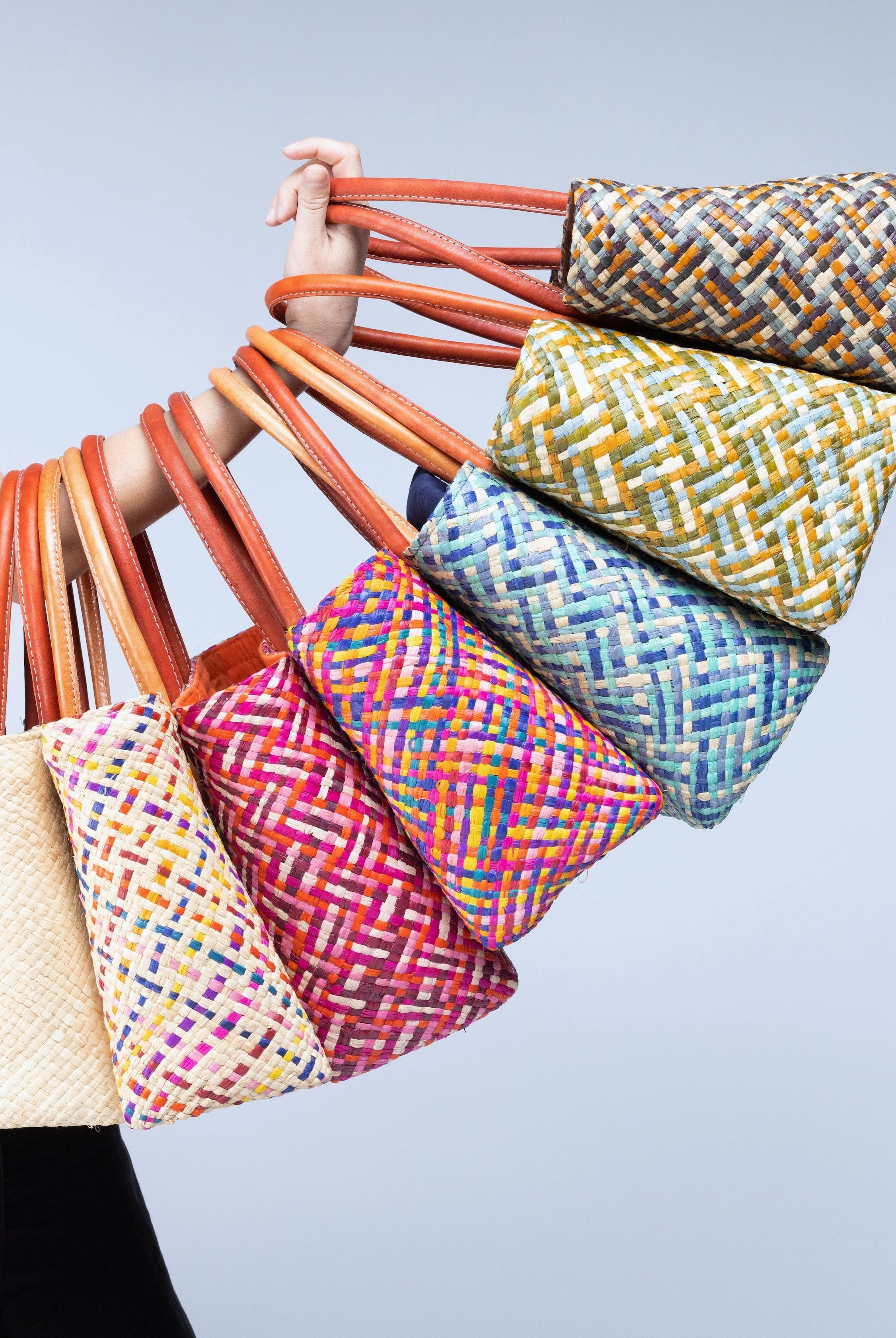 Model wearing multiple color options of Pianina Small Straw Basket Bags handmade from woven natural raffia palm fiber in a multicolor cross weave patterns handbag purse with leather handles - Shebobo