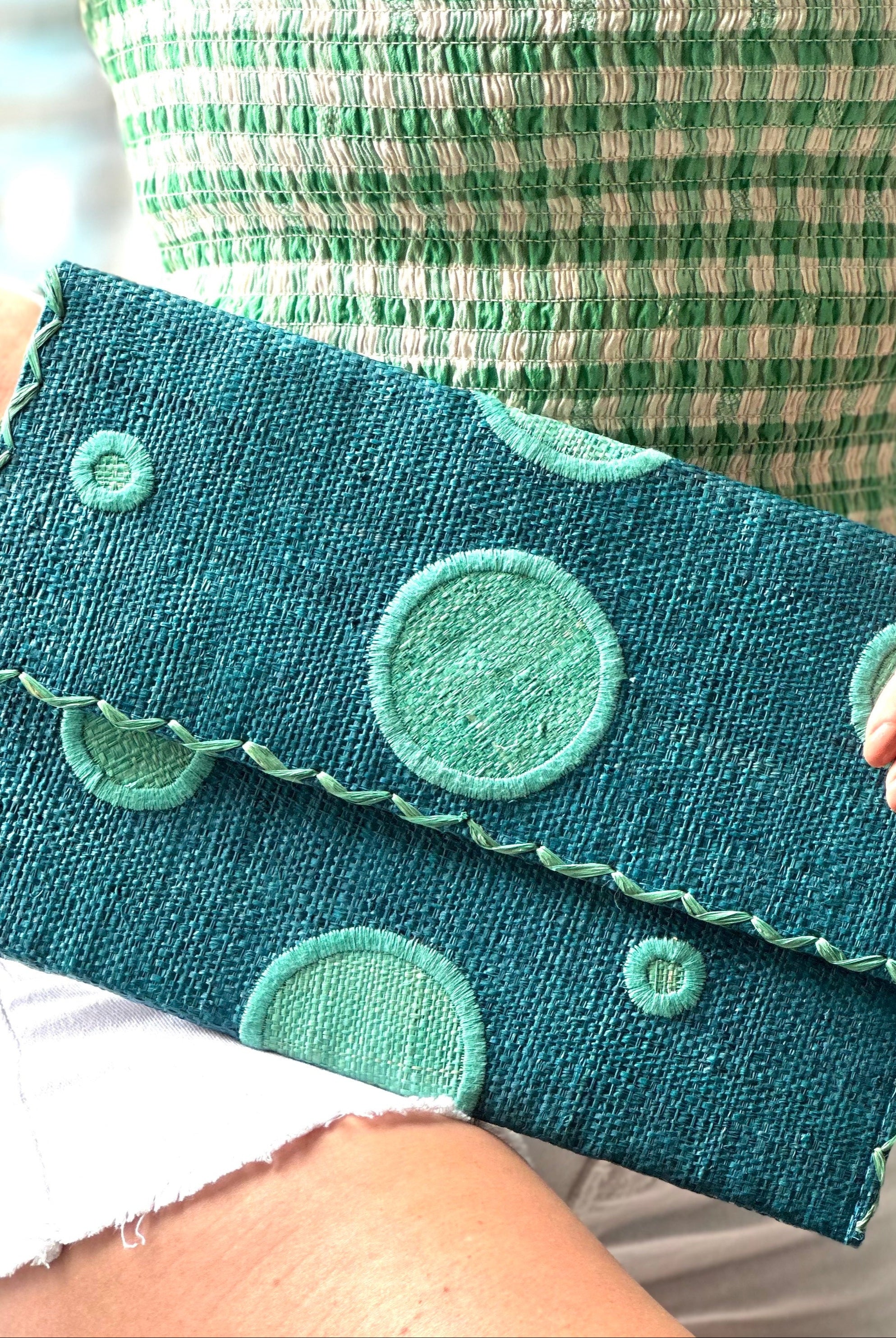 Model wearing Polka Dot Straw Clutch Handbag handmade loomed raffia clutch purse in multisize dot pattern of seafoam green/blue with matching color cross stitch edging on turquoise blue straw color purse - Shebobo