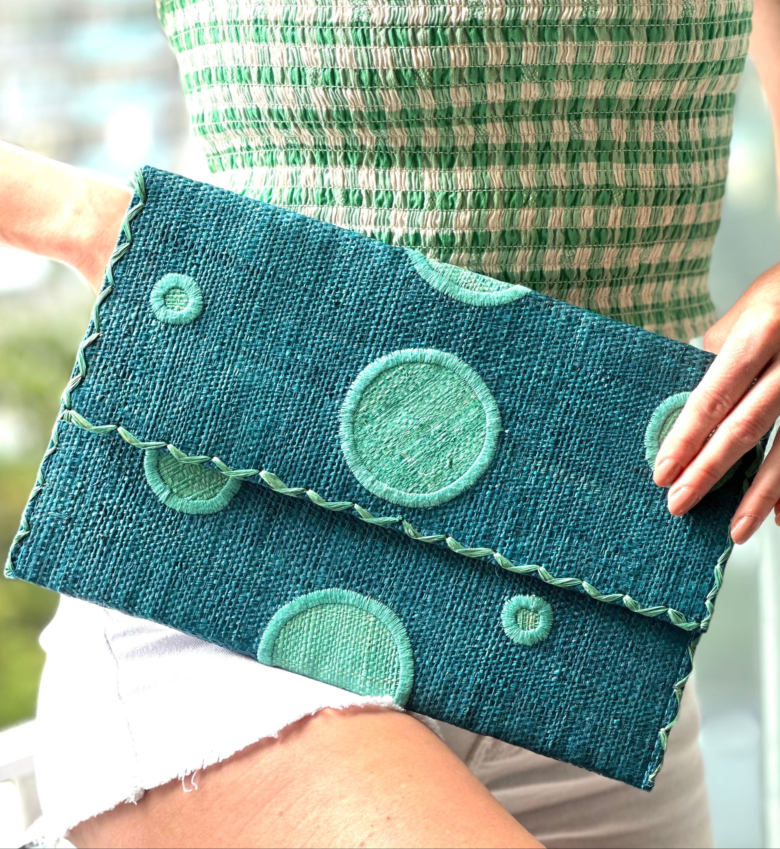 Model wearing Polka Dot Straw Clutch Handbag handmade loomed raffia clutch purse in multisize dot pattern of seafoam green/blue with matching color cross stitch edging on turquoise blue straw color purse - Shebobo