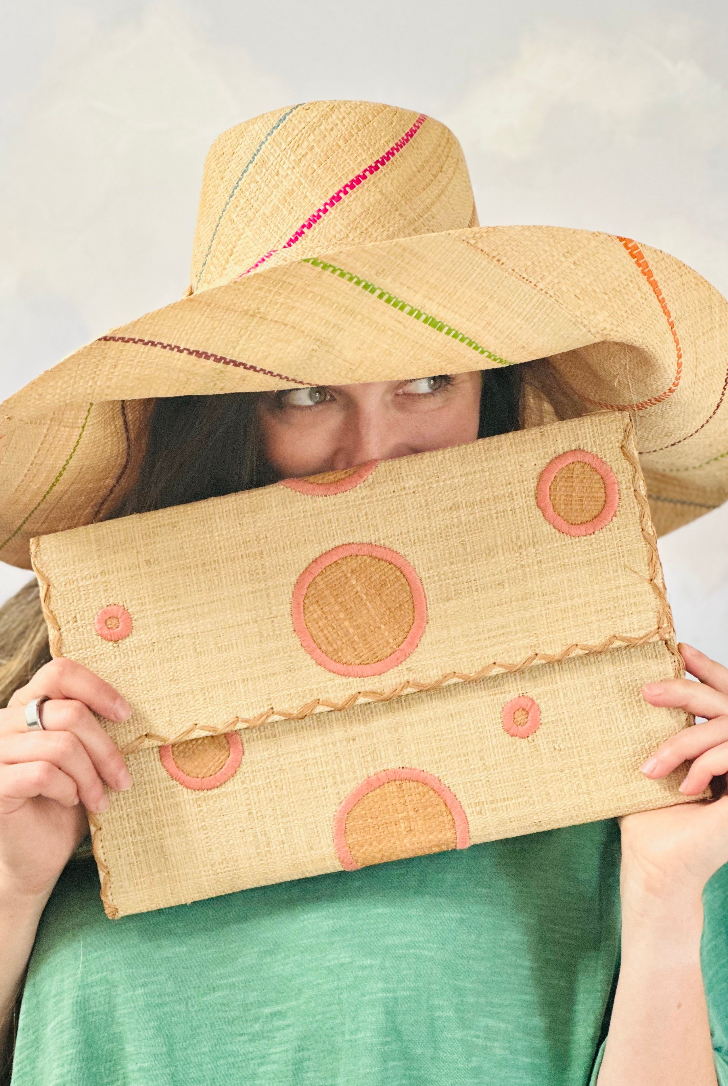Model wearing Polka Dot Straw Clutch Handbag handmade loomed raffia clutch purse in multisize dot pattern of blush orange/pink dots with matching color cross stitch edging on natural straw color purse- Shebobo (with Monica 5" & 7" Pinstripe Packable Straw Sun Hats)